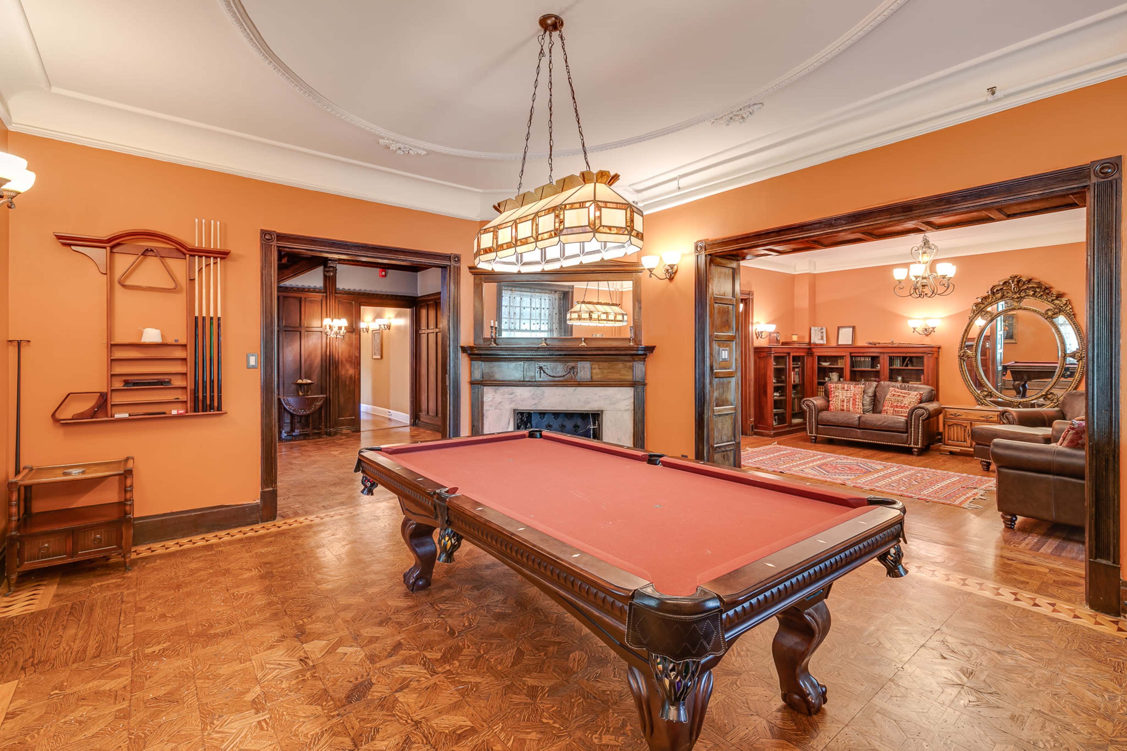 The image shows a room with a red billiards table centered under a chandelier, surrounded by walls painted orange and wooden accents.