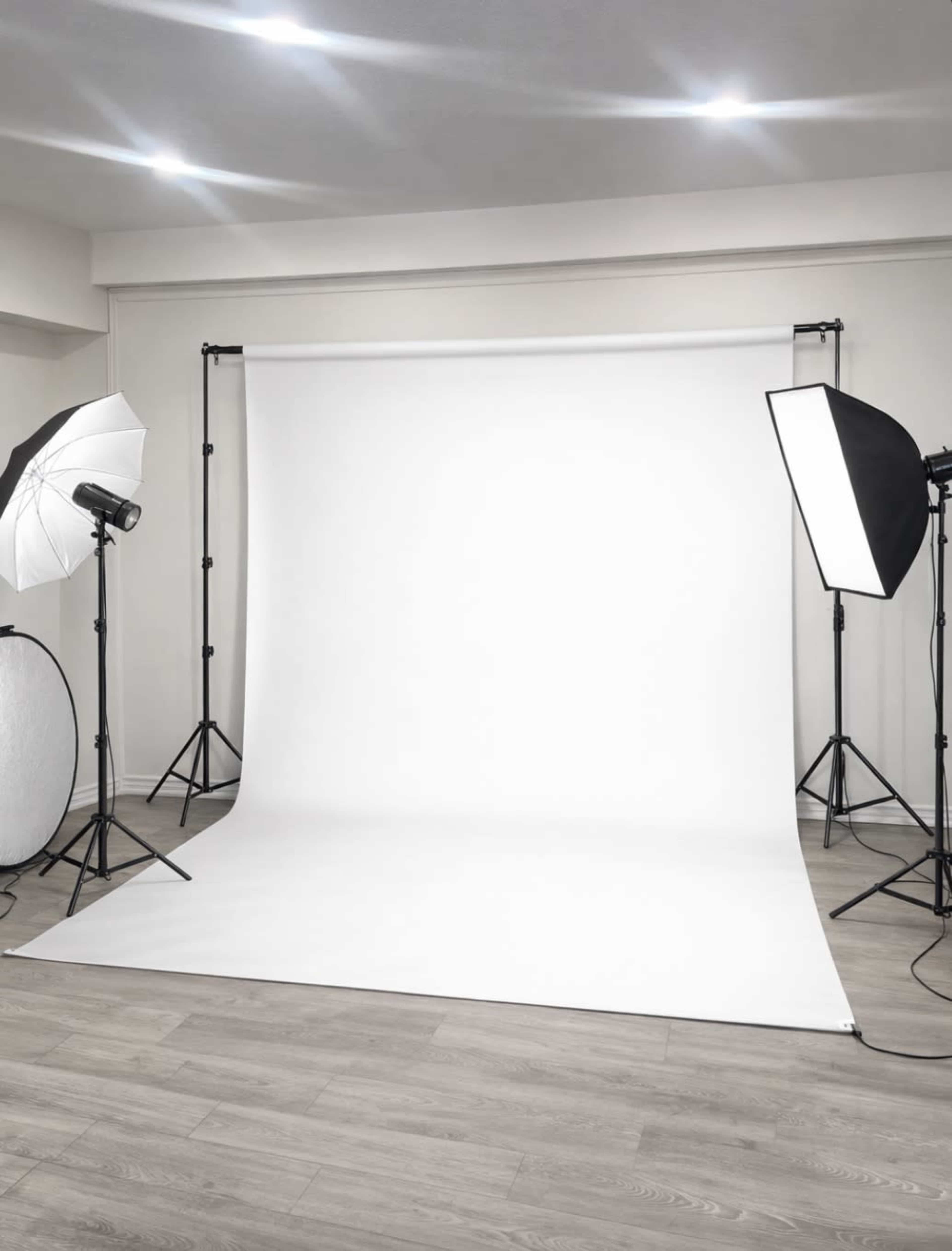 The image shows a photography studio setup with a white backdrop, lighting equipment, and reflectors arranged on the floor.