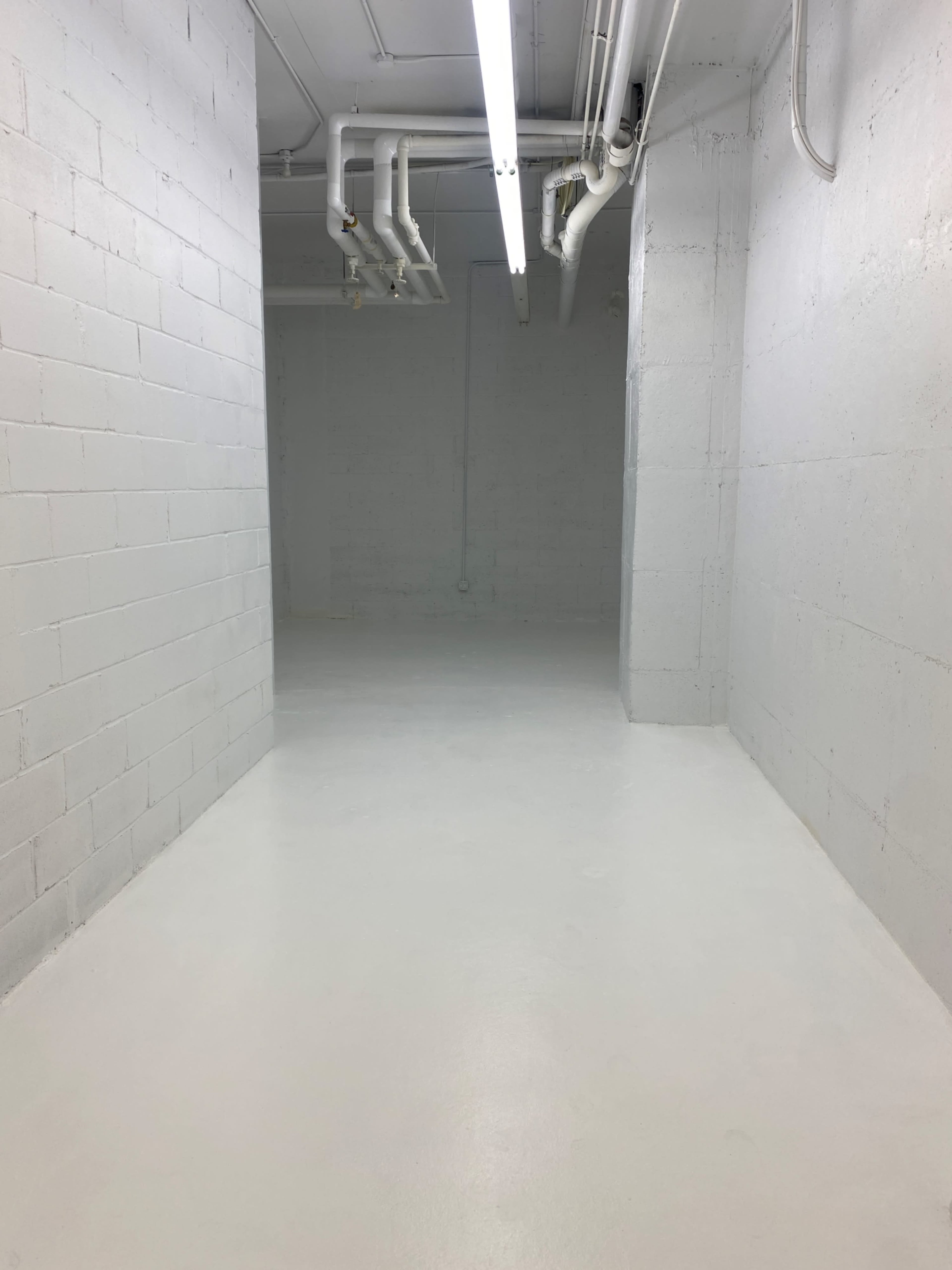 A long, empty corridor in a basement with gray concrete walls and a polished white floor.