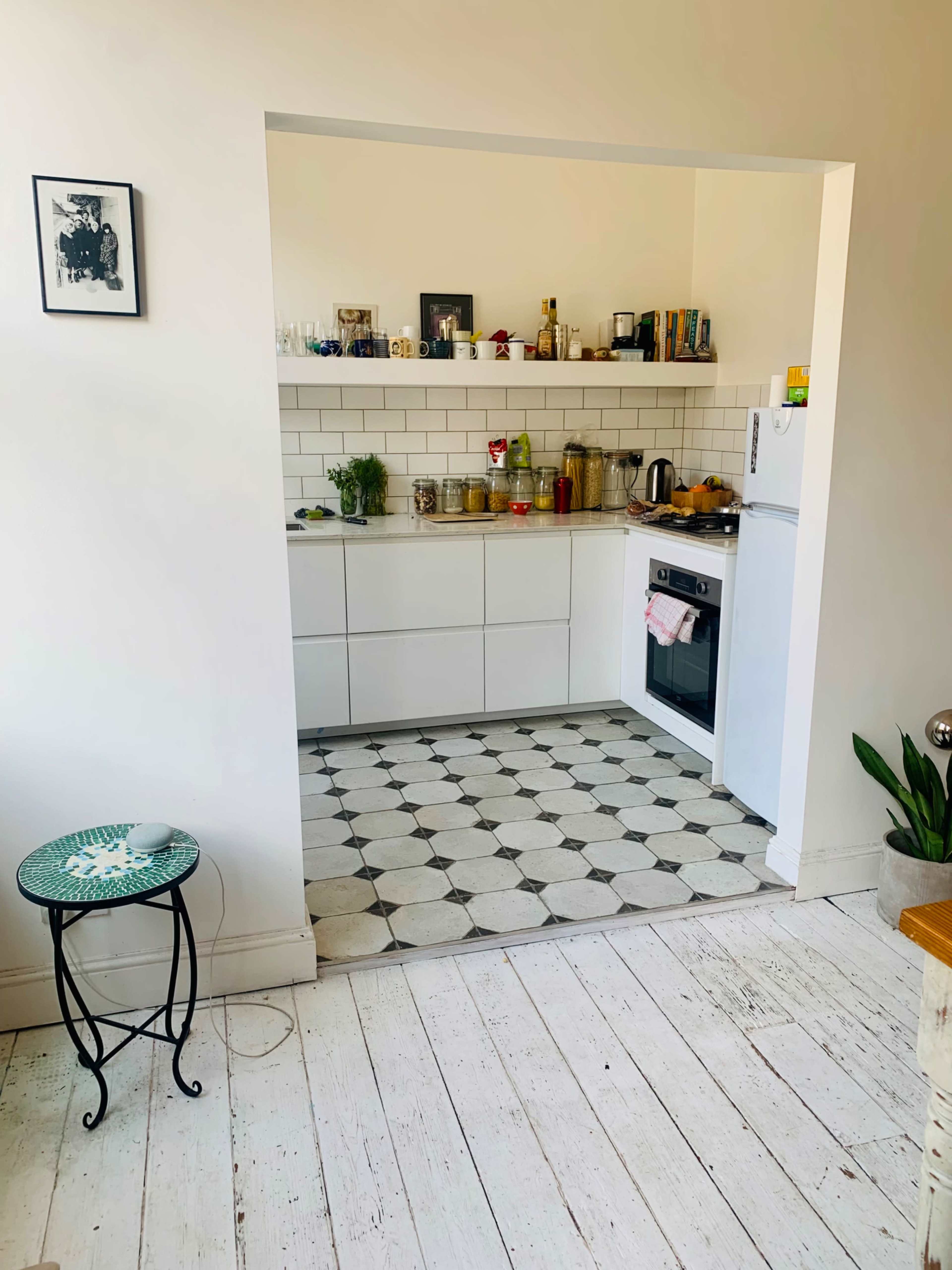 A clean kitchen features white cabinets, a tiled floor with circular patterns, and an opening that leads to a living area.