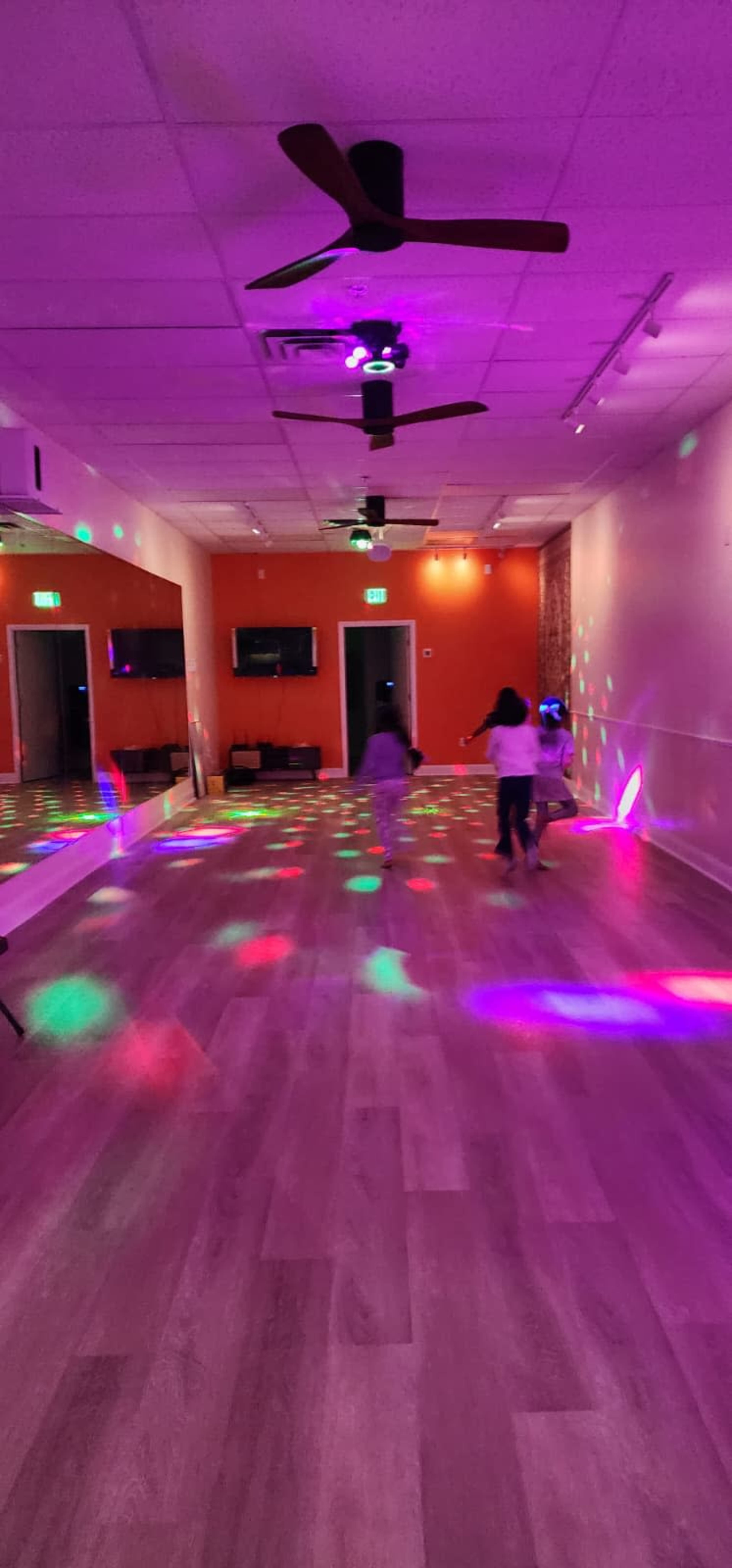 A brightly lit dance studio features colorful lights casting patterns on the floor as two children play in the background.