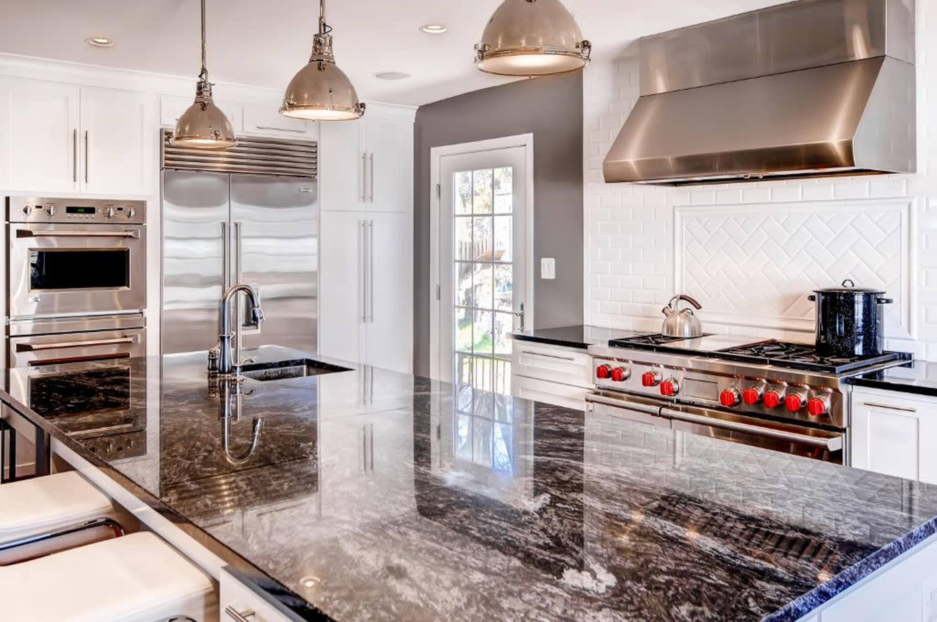 A modern kitchen featuring stainless steel appliances, a large granite island, and a gas stove with red knobs.