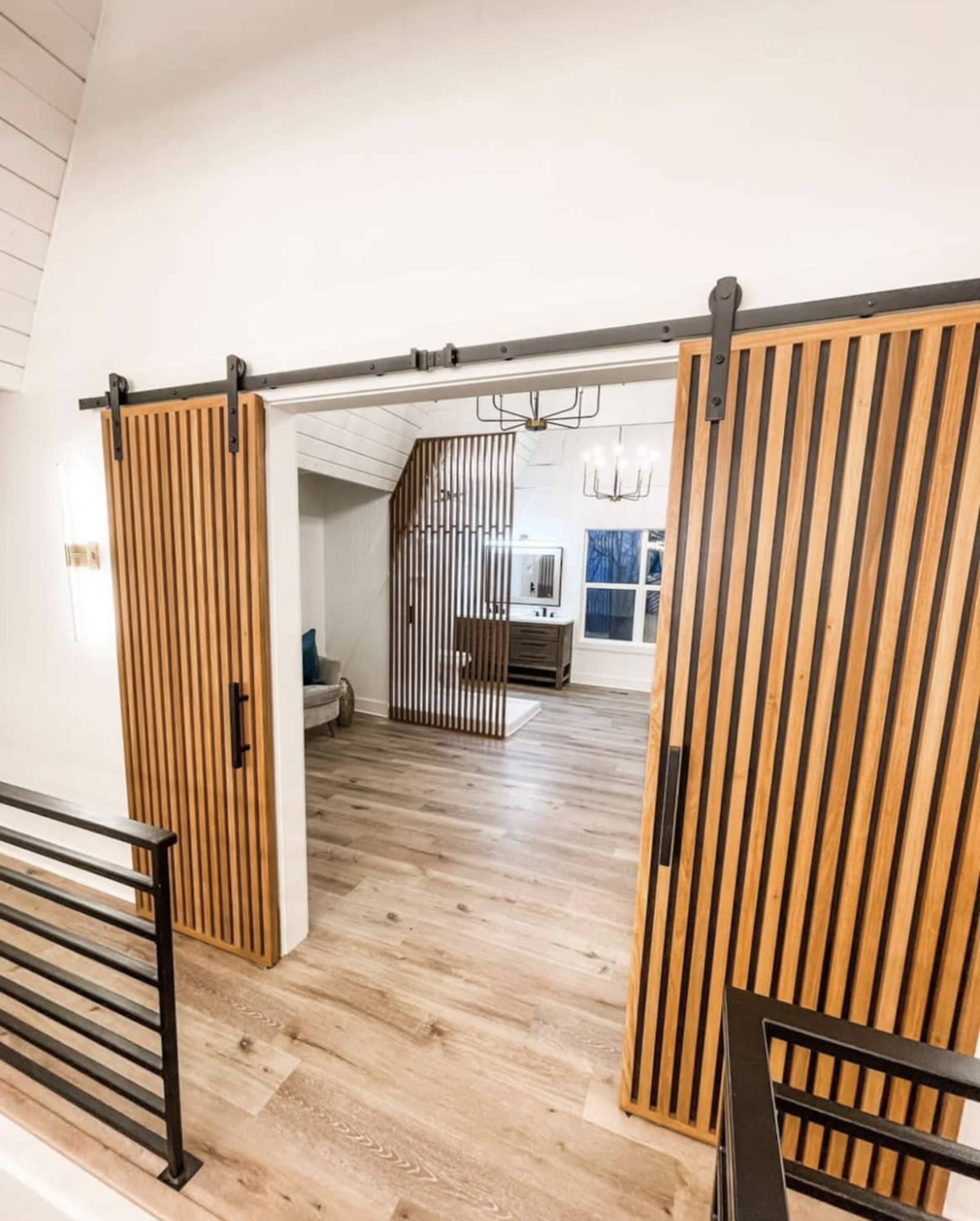 A modern interior with wooden sliding barn doors leading to a room featuring wooden flooring and a staircase.