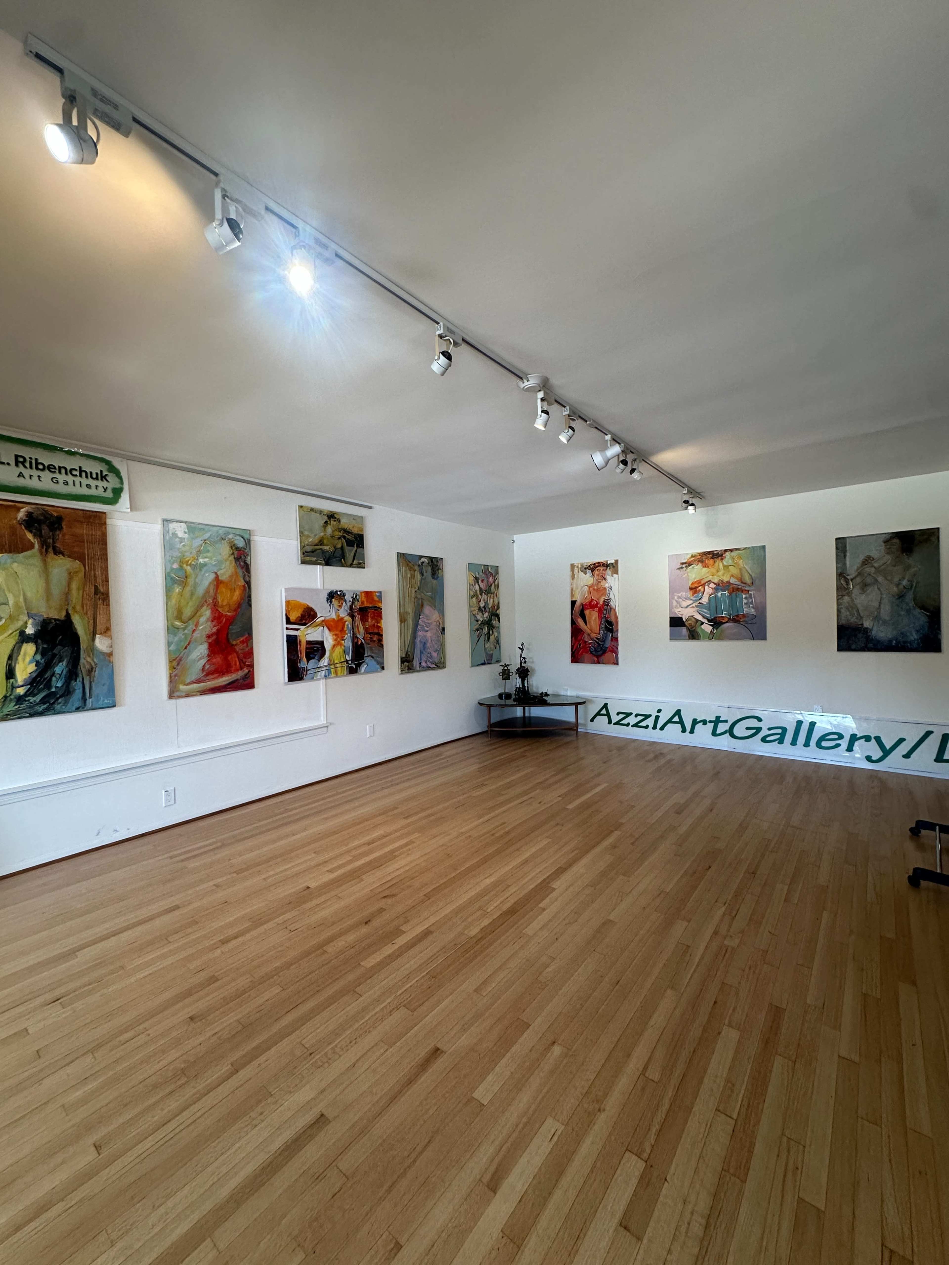 The image shows an art gallery with several abstract paintings displayed on the walls and wooden flooring.