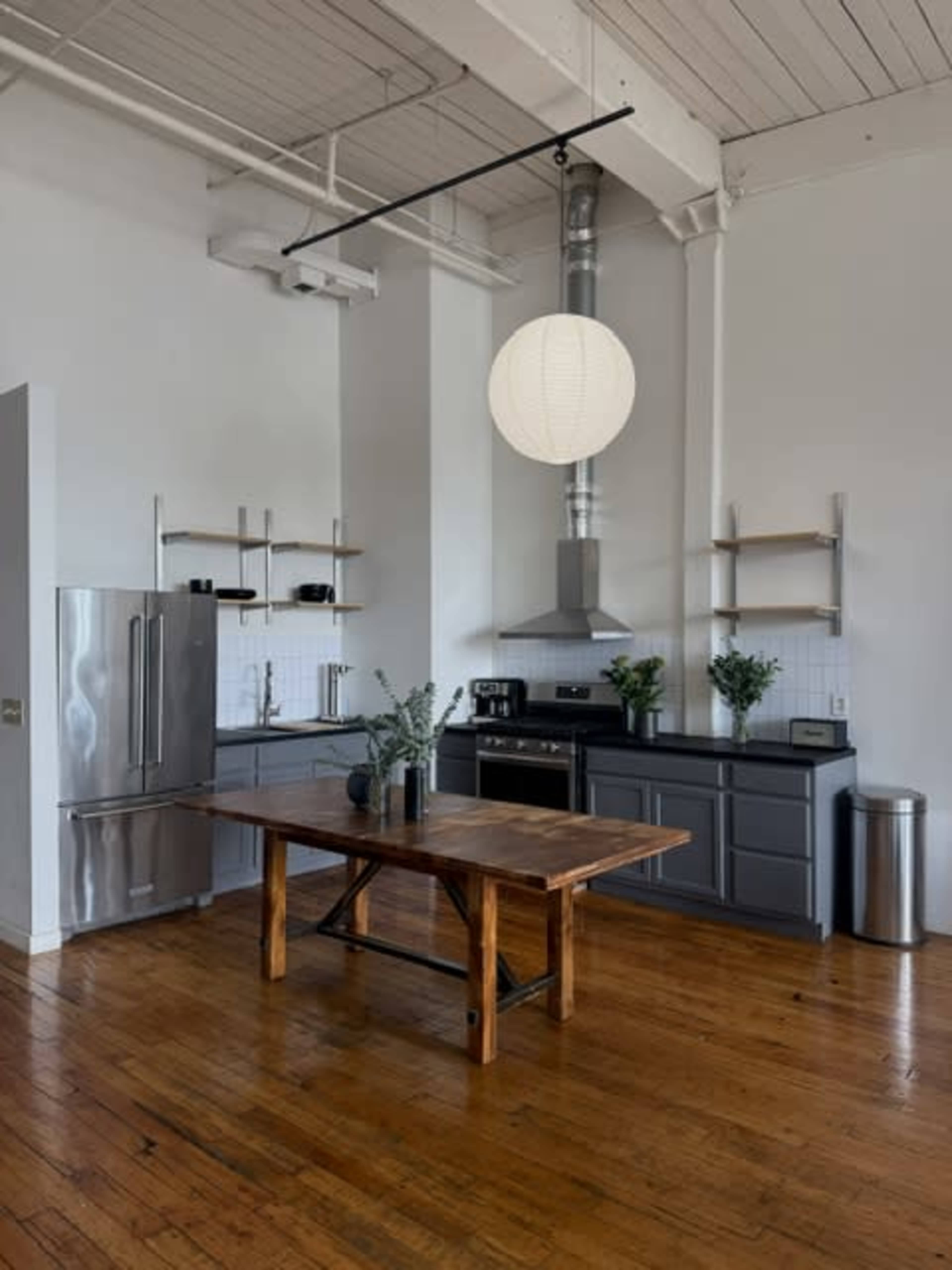 The image features a modern kitchen with stainless steel appliances, dark cabinetry, a wooden dining table, and a pendant light, all set against a backdrop of hardwood floors.