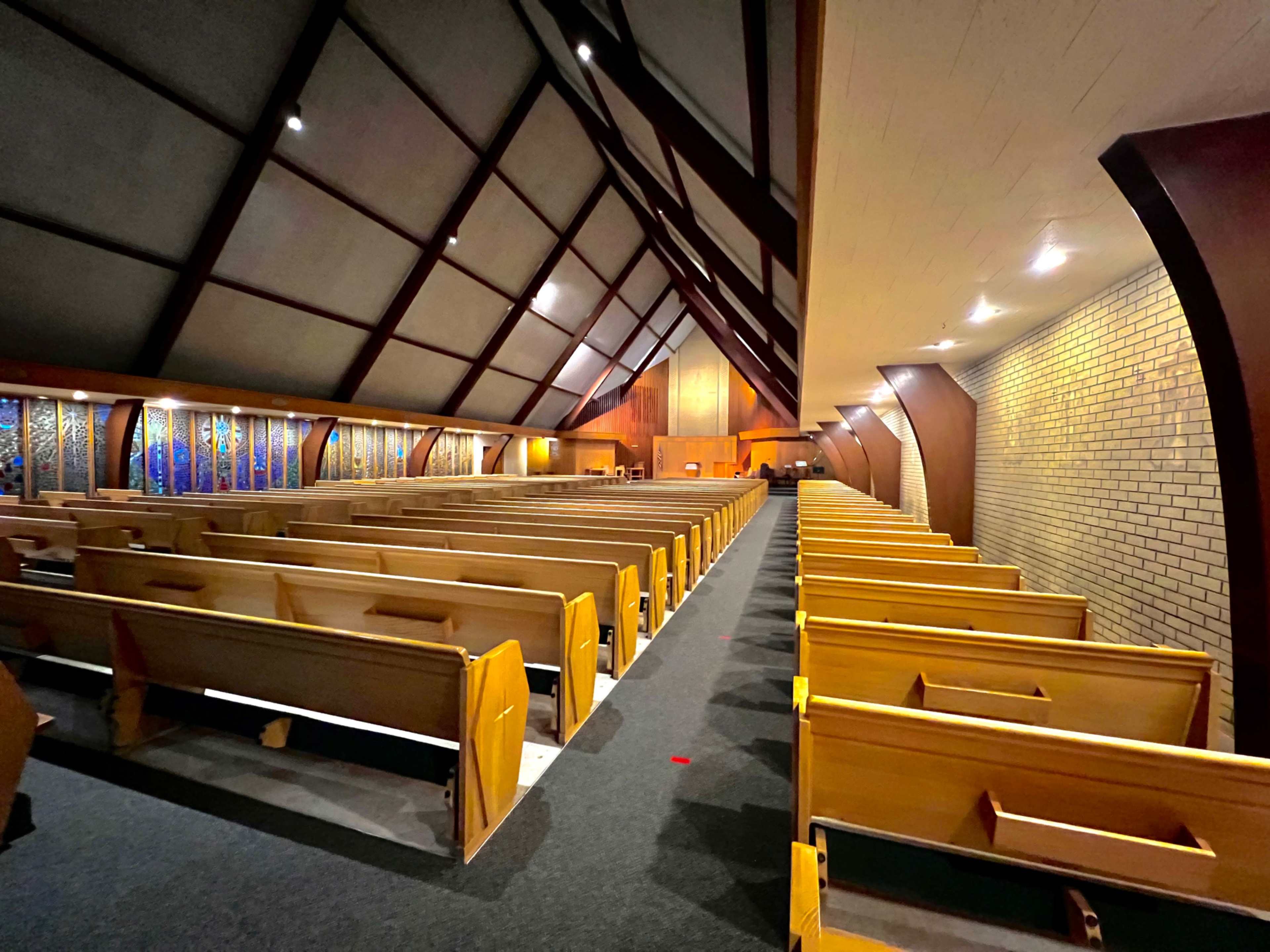 The image shows the interior of a church with wooden pews arranged in rows and a high, sloped ceiling.
