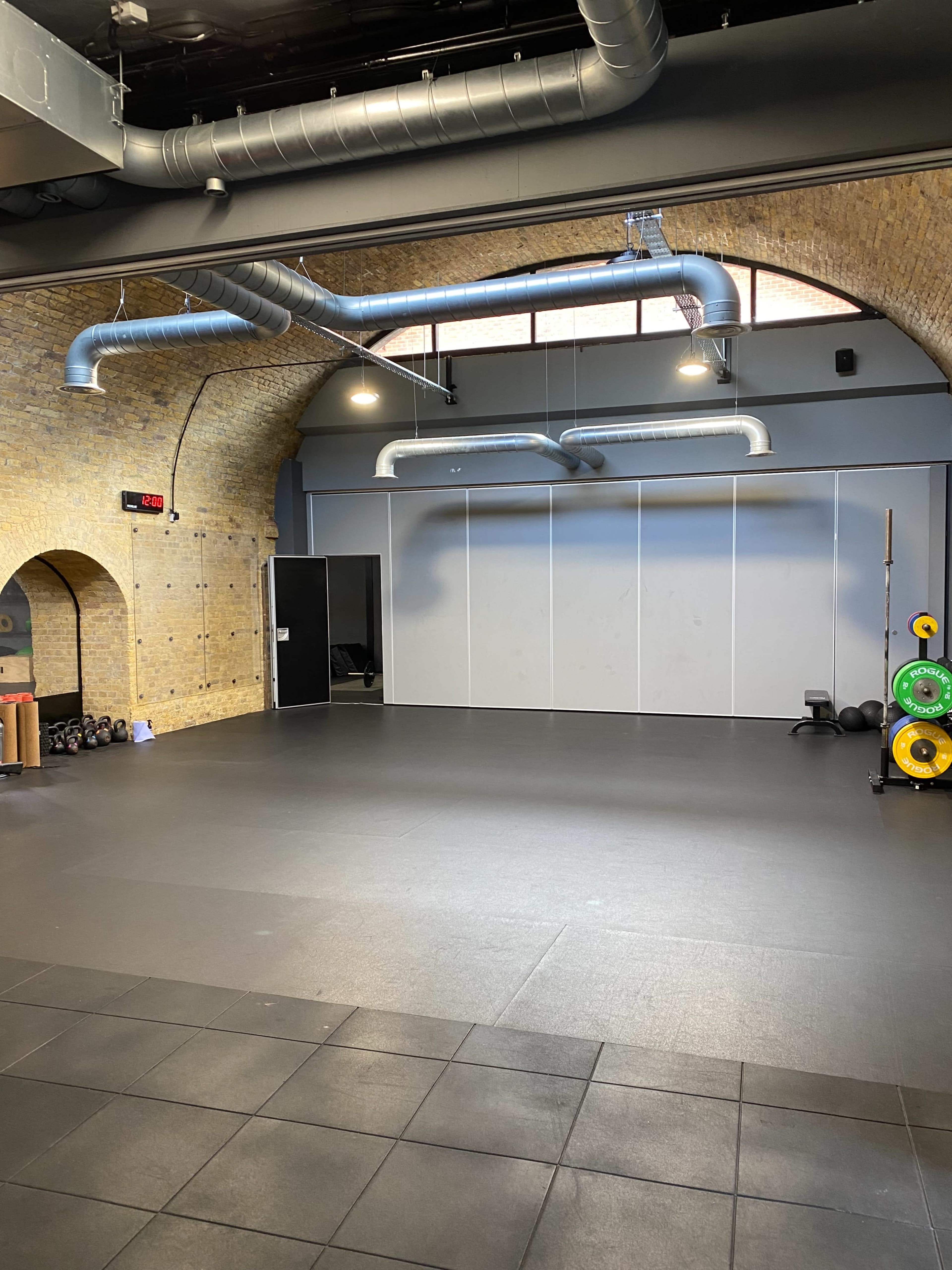 A spacious gym interior with arched brick walls, gray flooring, and equipment arranged along one side.