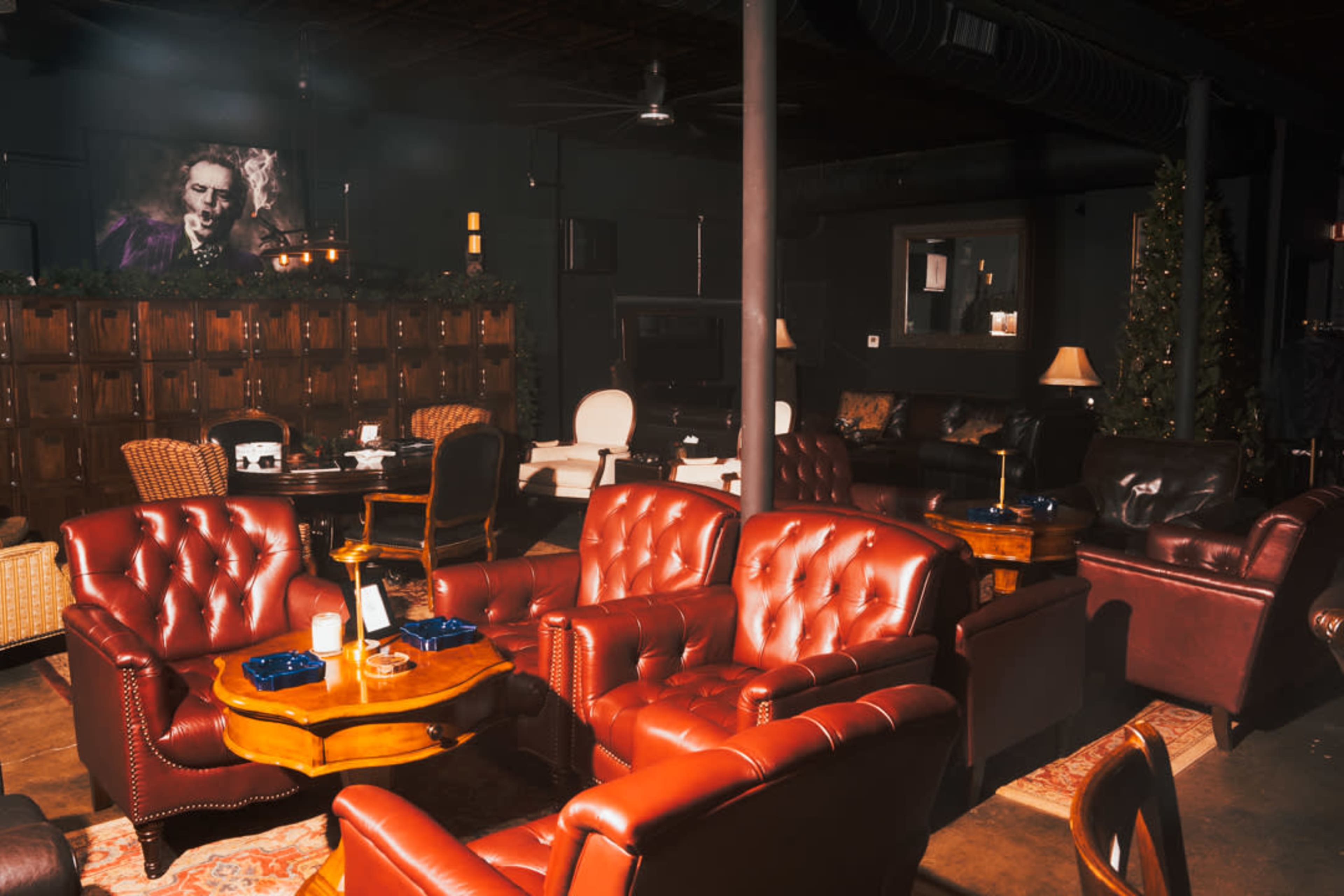 The image depicts a cozy lounge area with leather armchairs and wooden tables, featuring dim lighting and dark walls.