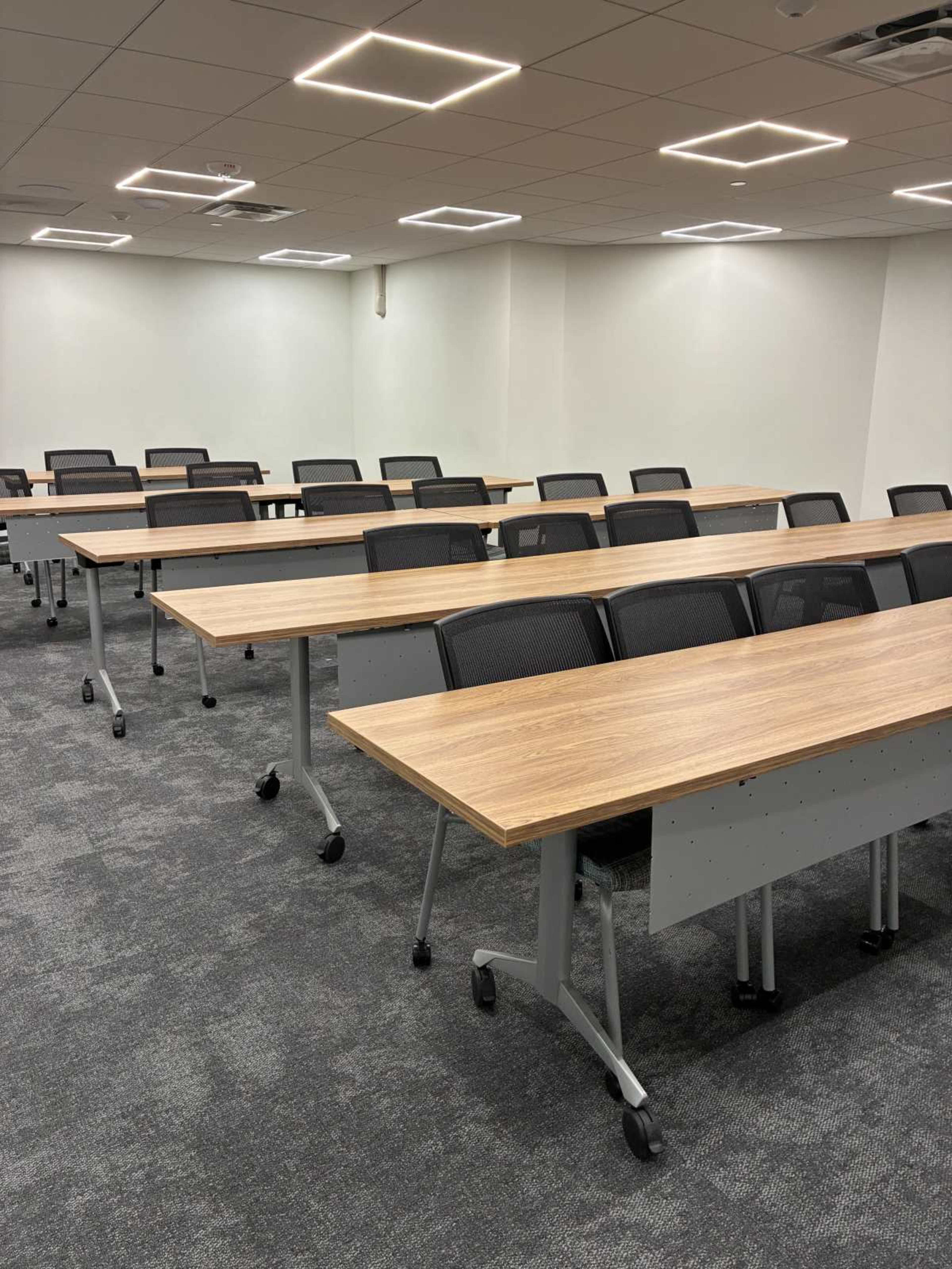 The image shows a conference room with multiple rows of adjustable tables and office chairs arranged in a grid pattern.