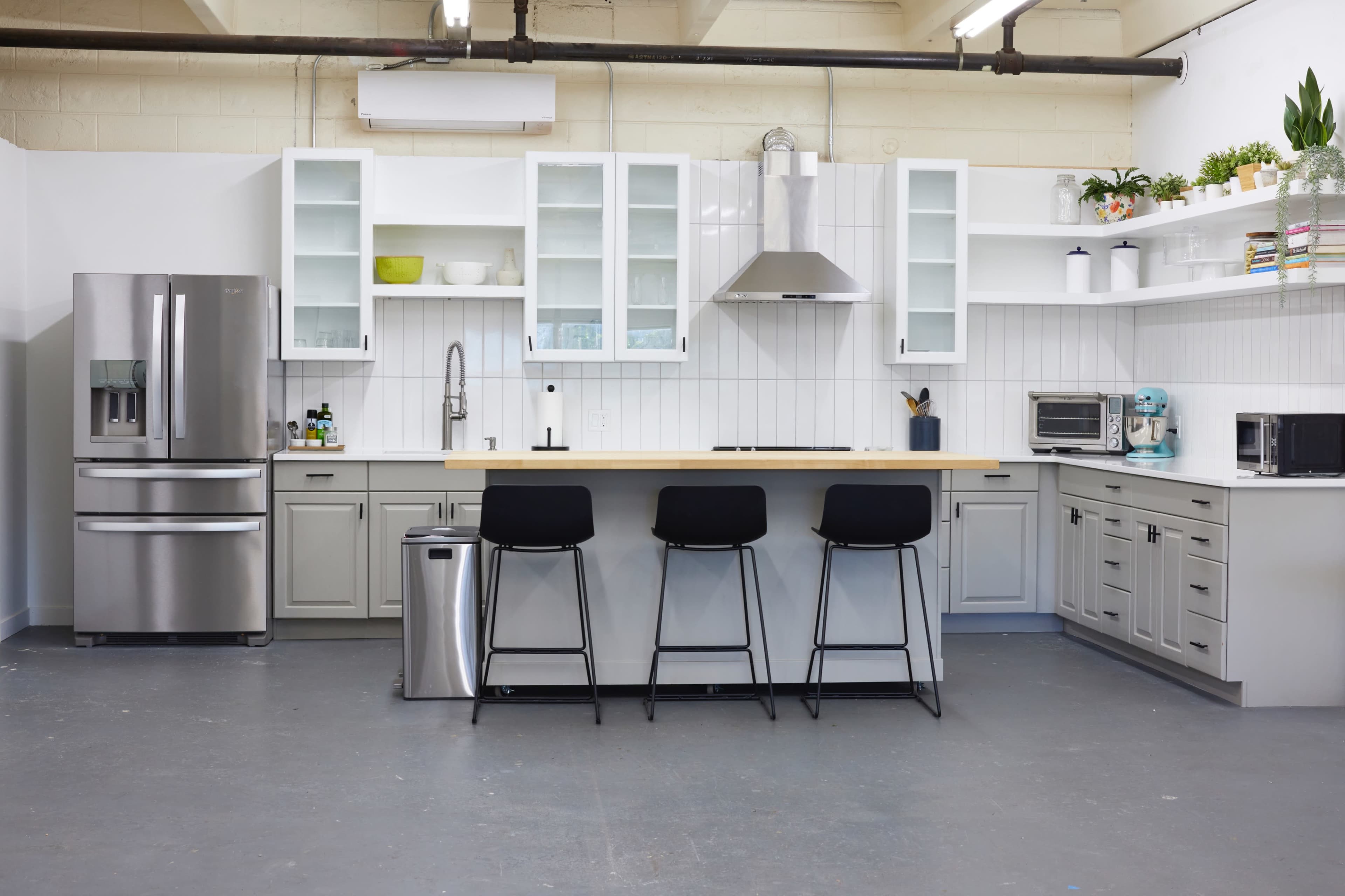 A modern kitchen features gray cabinetry, stainless steel appliances, a central island with bar stools, and open shelves displaying dishware.