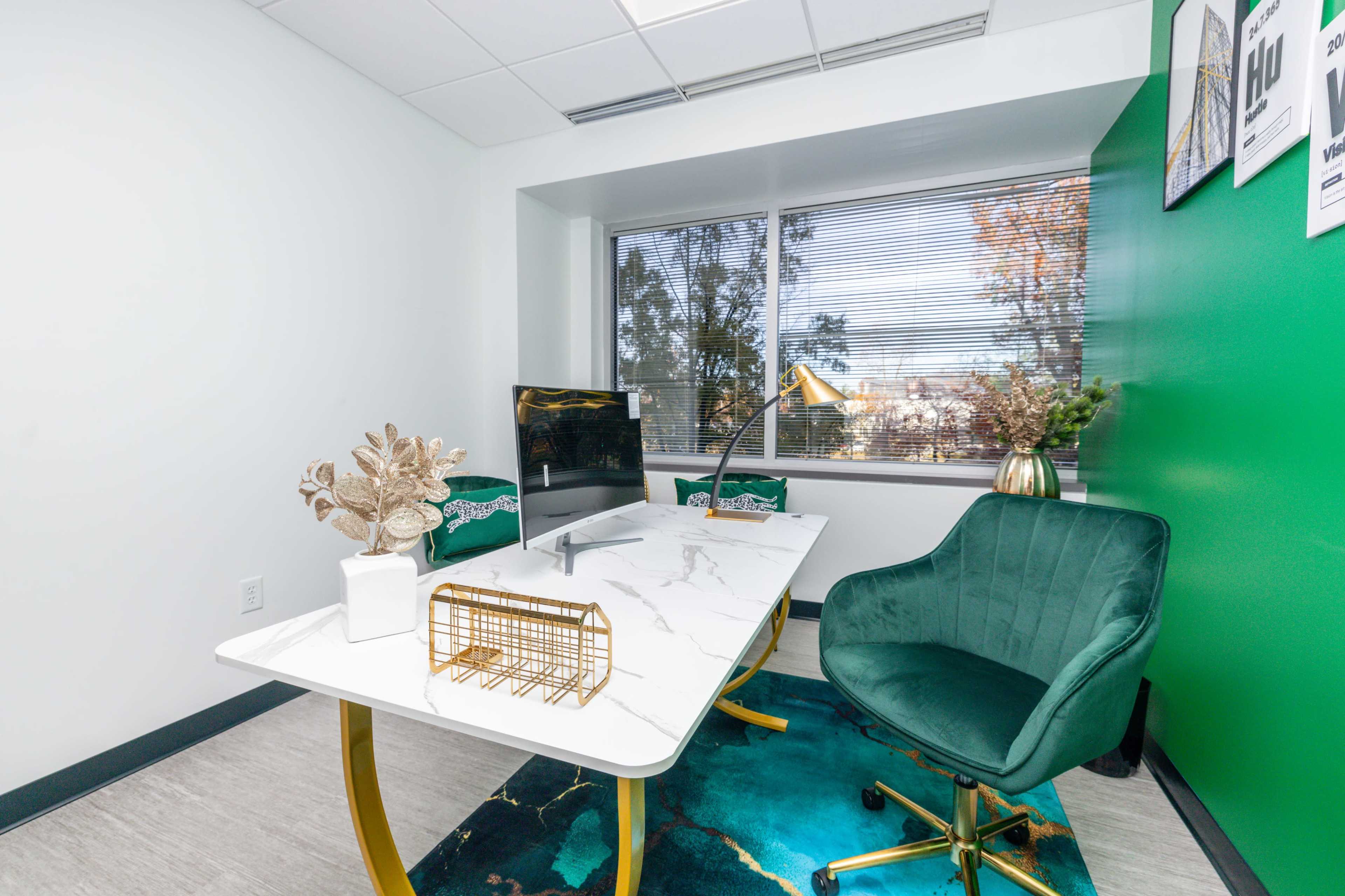 A modern office with a marble-top desk, a green velvet chair, and a large window overlooking a tree-filled exterior.