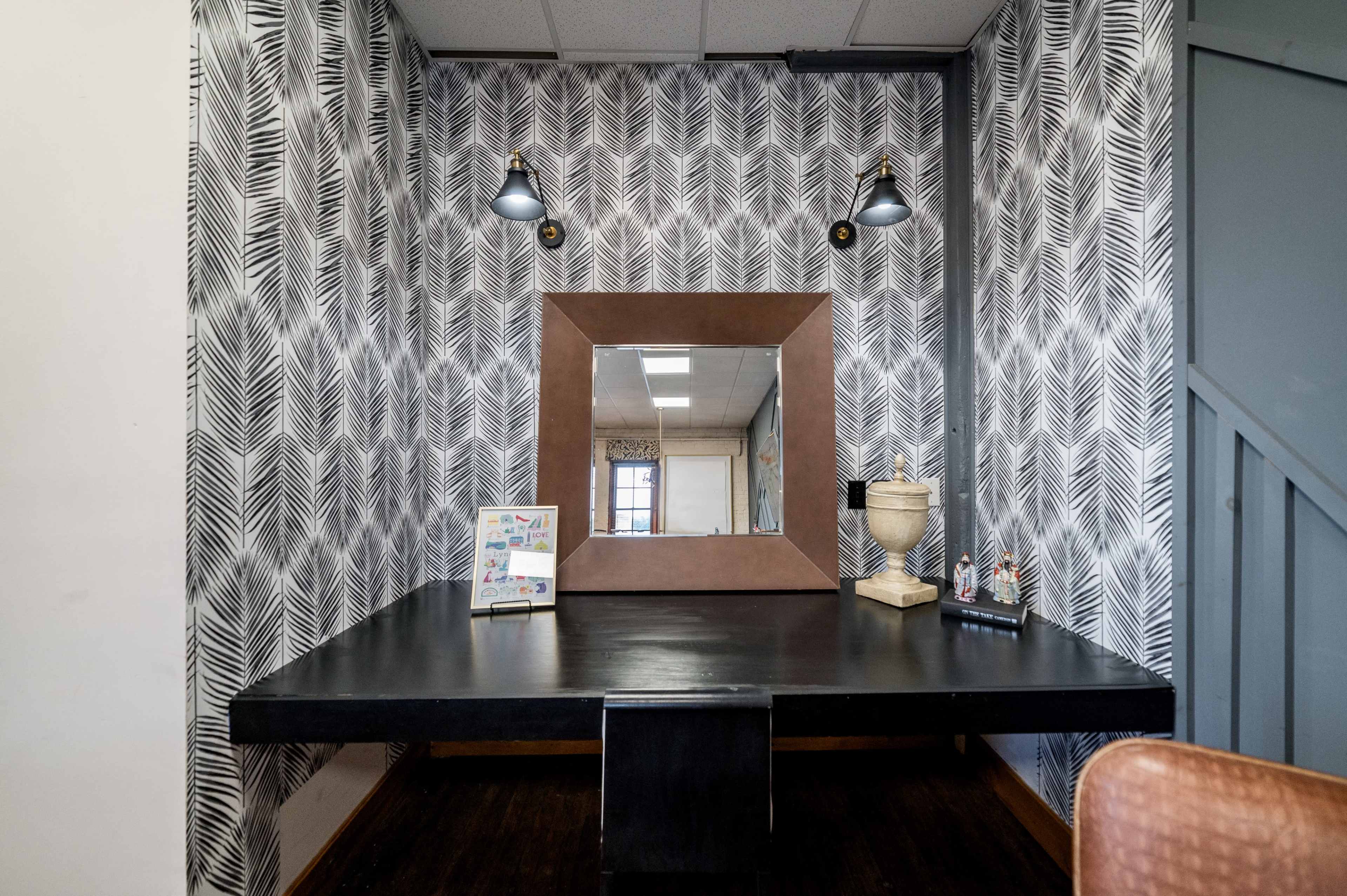 A room with a textured wallpaper featuring a leaf pattern, a dark table with a large mirror above it, and decorative items on the table.