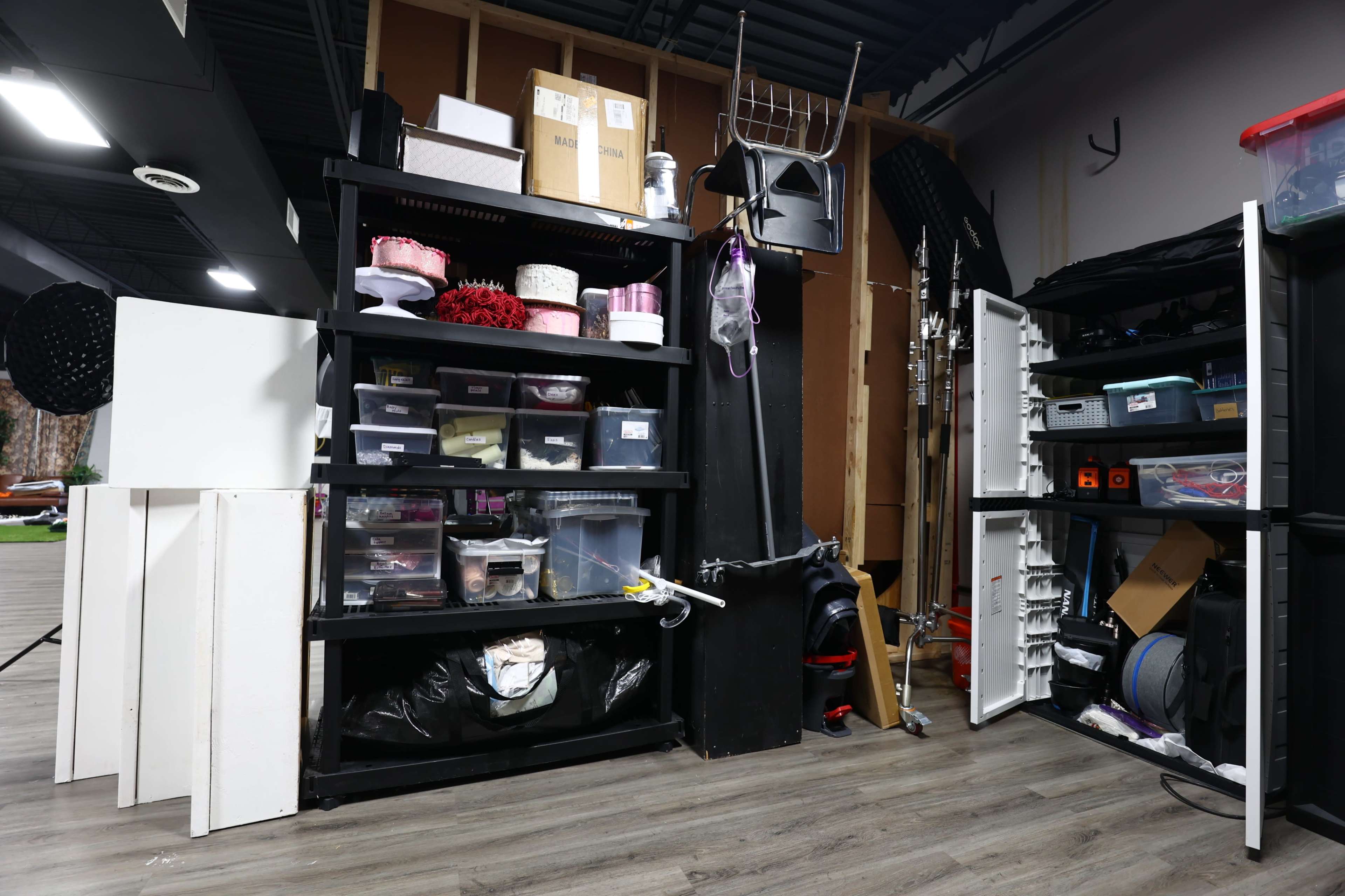 The image shows a cluttered storage area with shelves containing various boxes, containers, and equipment in a semi-organized manner.