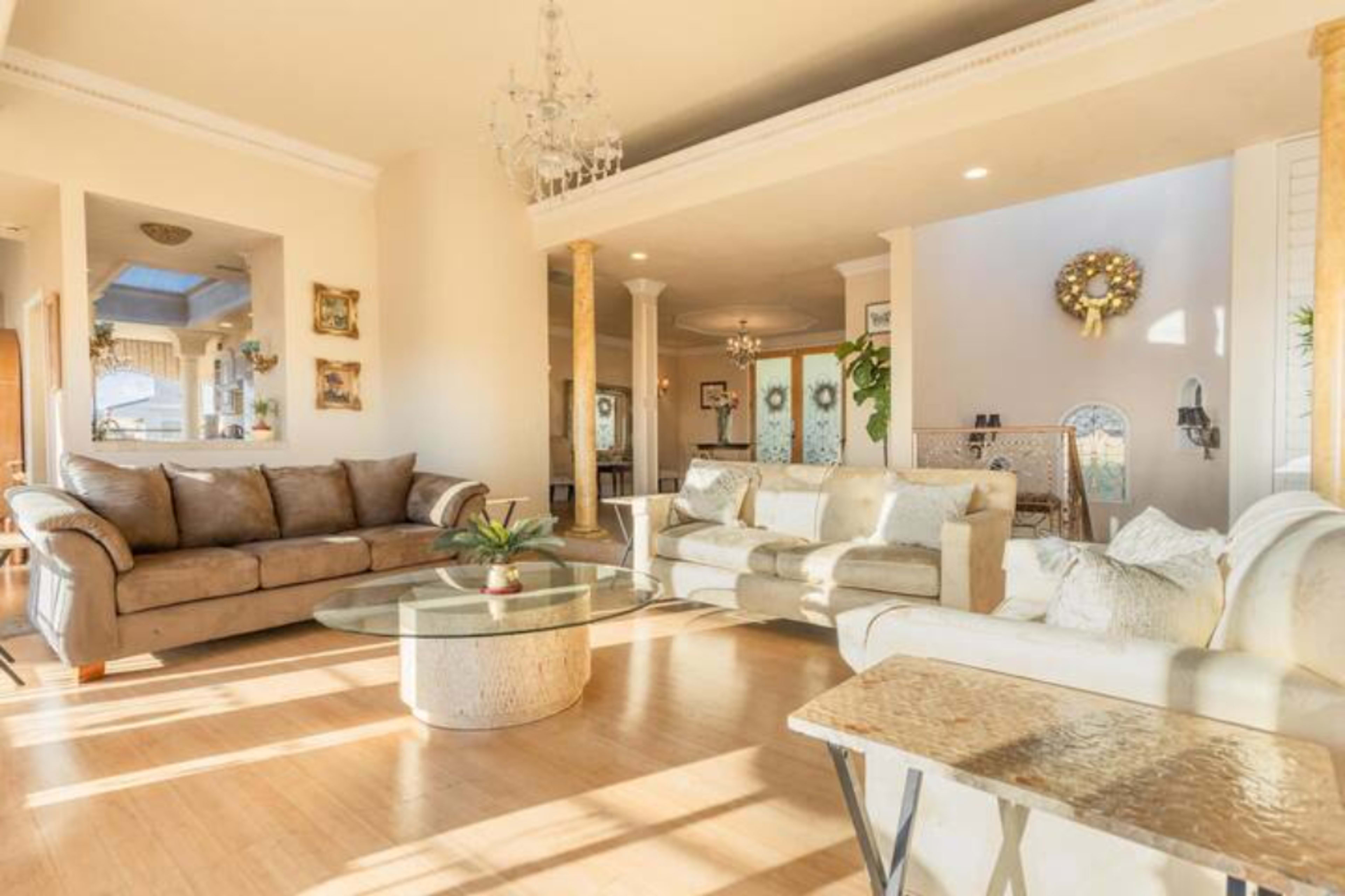 A bright living room features two sofas, a glass coffee table, and a chandelier, with decorative elements in the background.