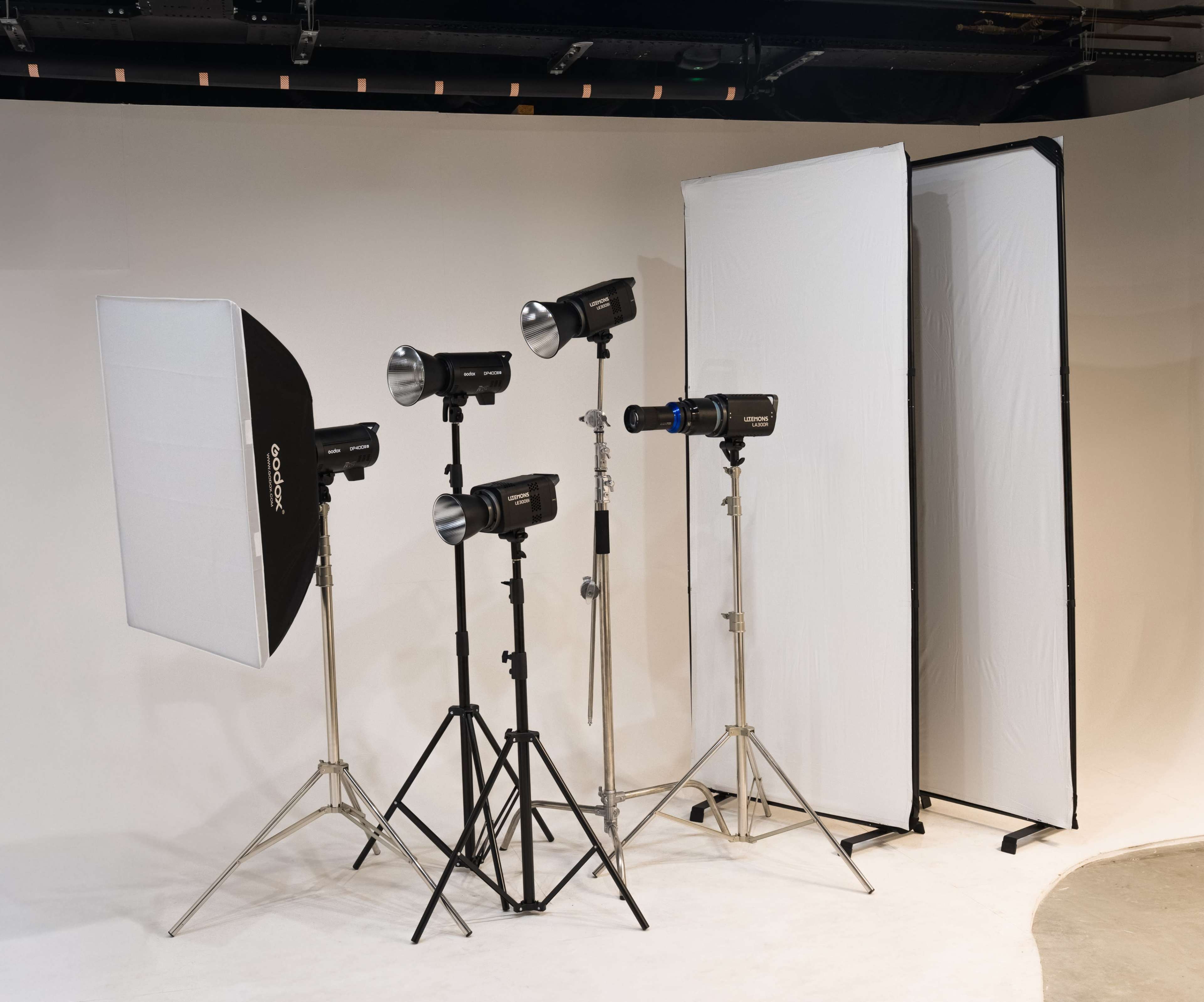 The image shows a photography studio setup featuring multiple light fixtures, softboxes, and diffusion panels positioned on tripods against a neutral backdrop.
