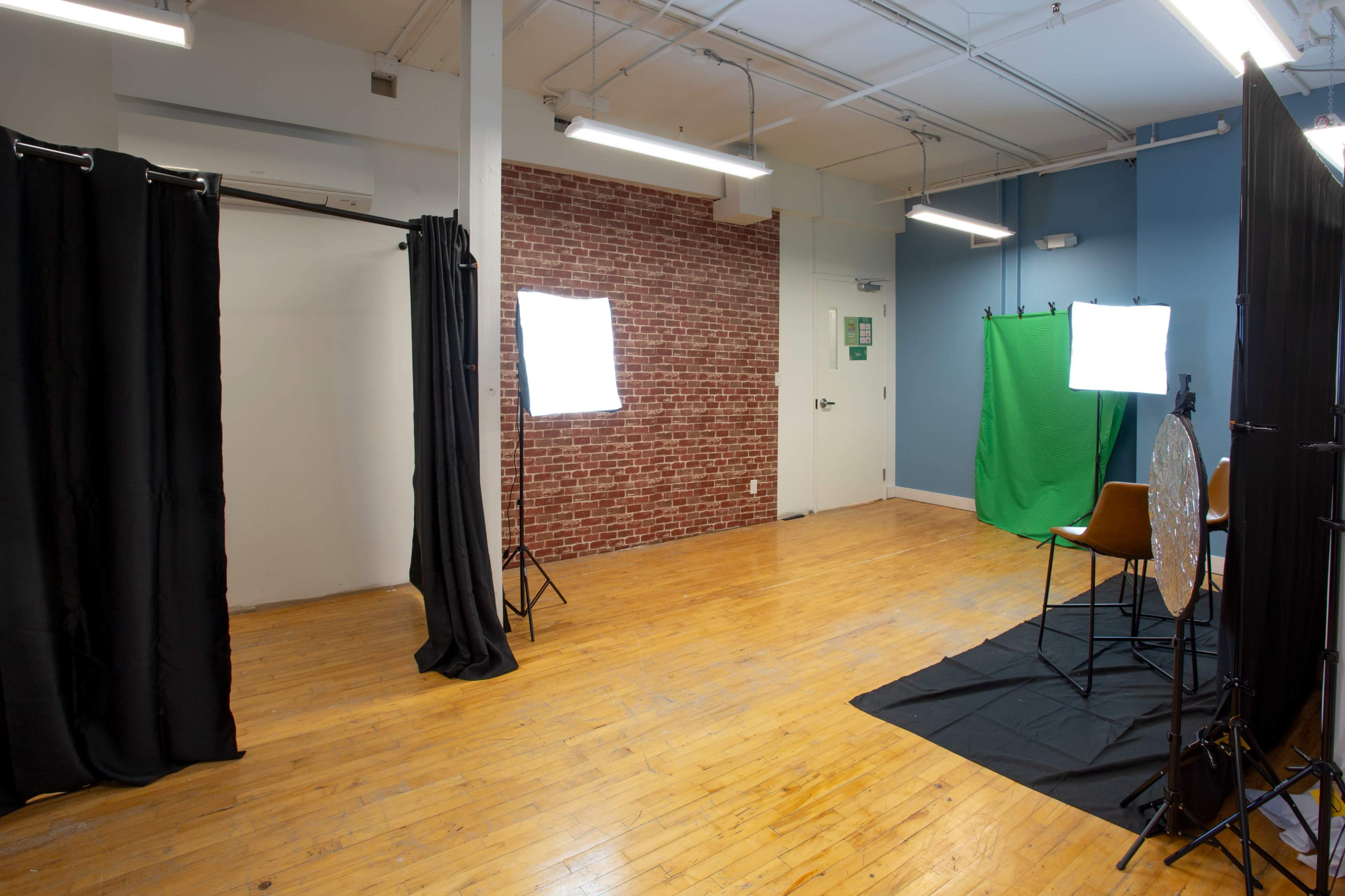 A spacious studio with a wooden floor, two backdrop areas, lighting equipment, and a green screen setup.