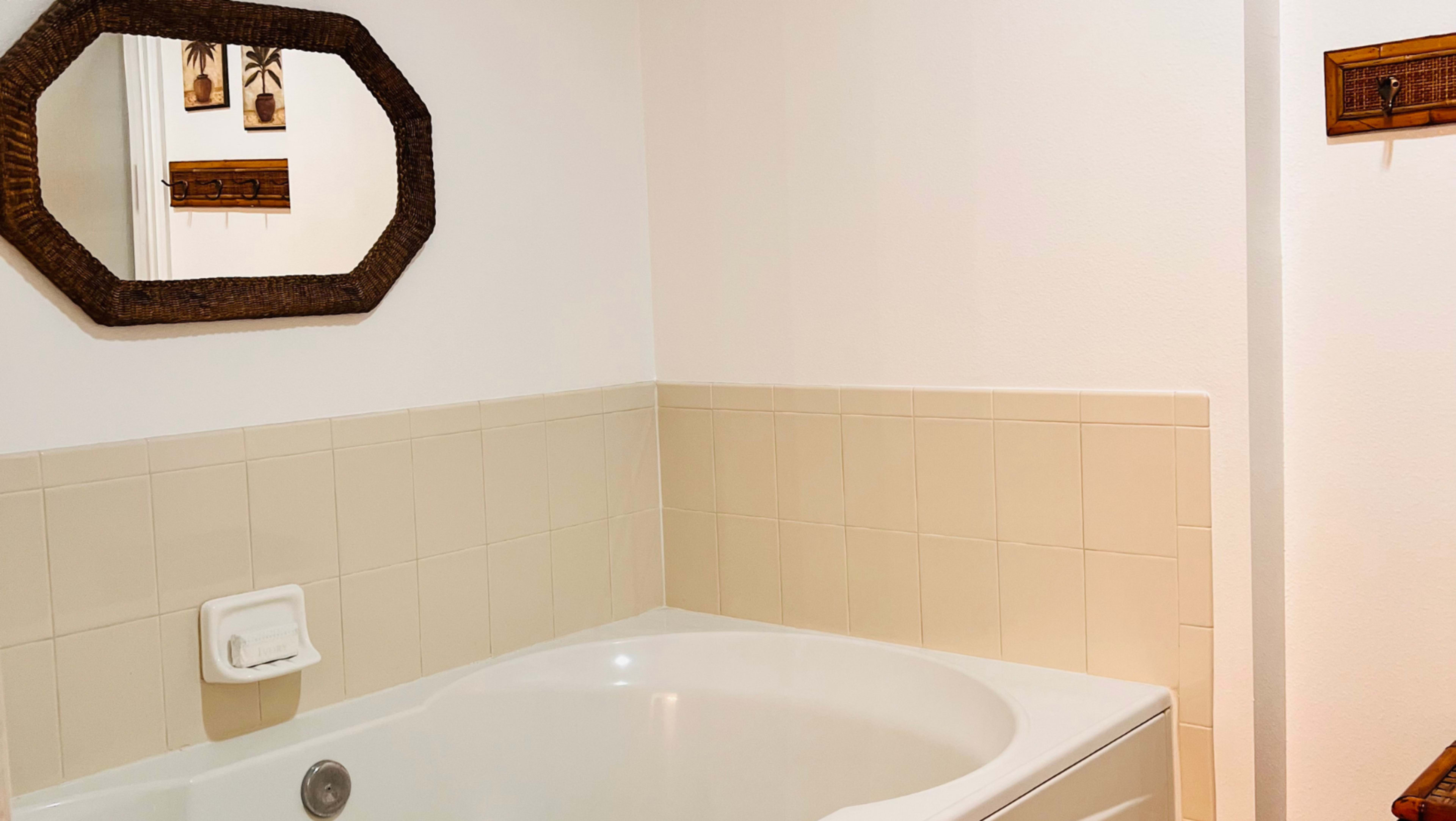 A bathroom with a white bathtub, beige tiled walls, and a rectangular mirror above the tub.