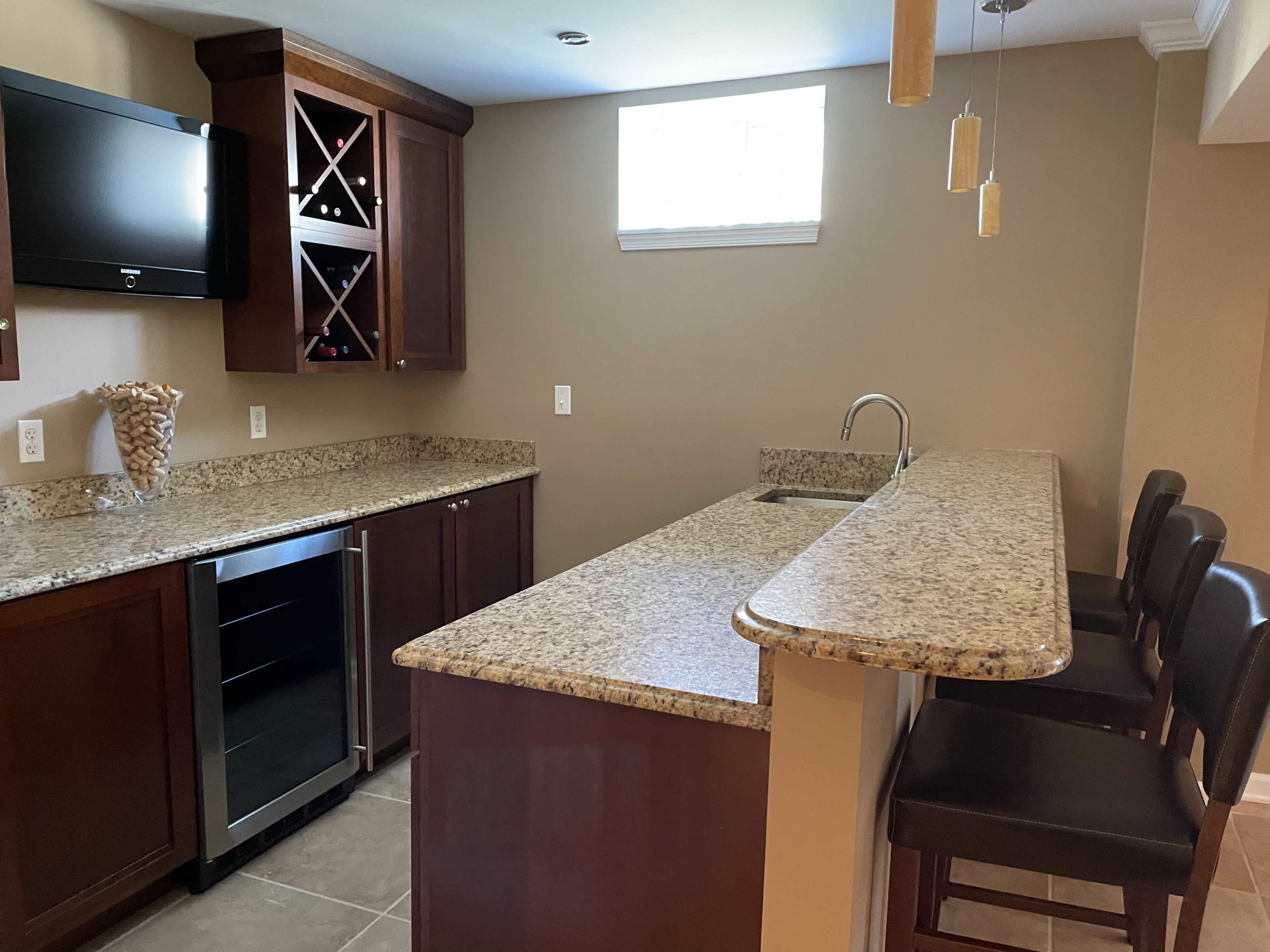 A modern kitchen with wooden cabinetry, a granite countertop, a wine cooler, and bar seating.