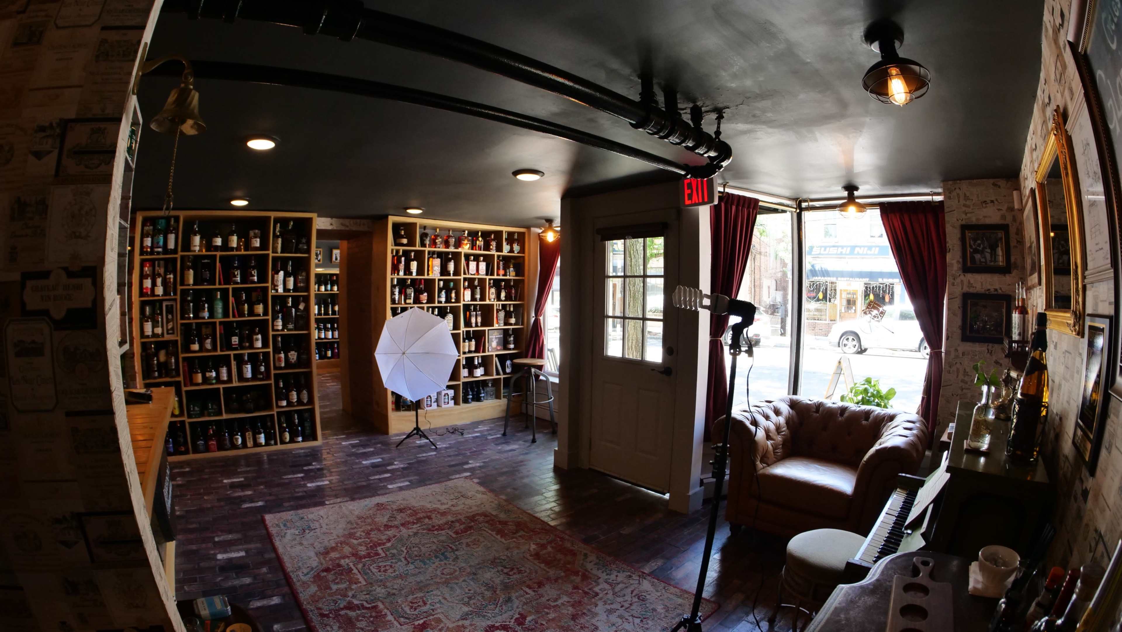A well-lit room features shelves filled with bottles, a vintage leather sofa, a white umbrella reflector, and a doorway leading to the street.