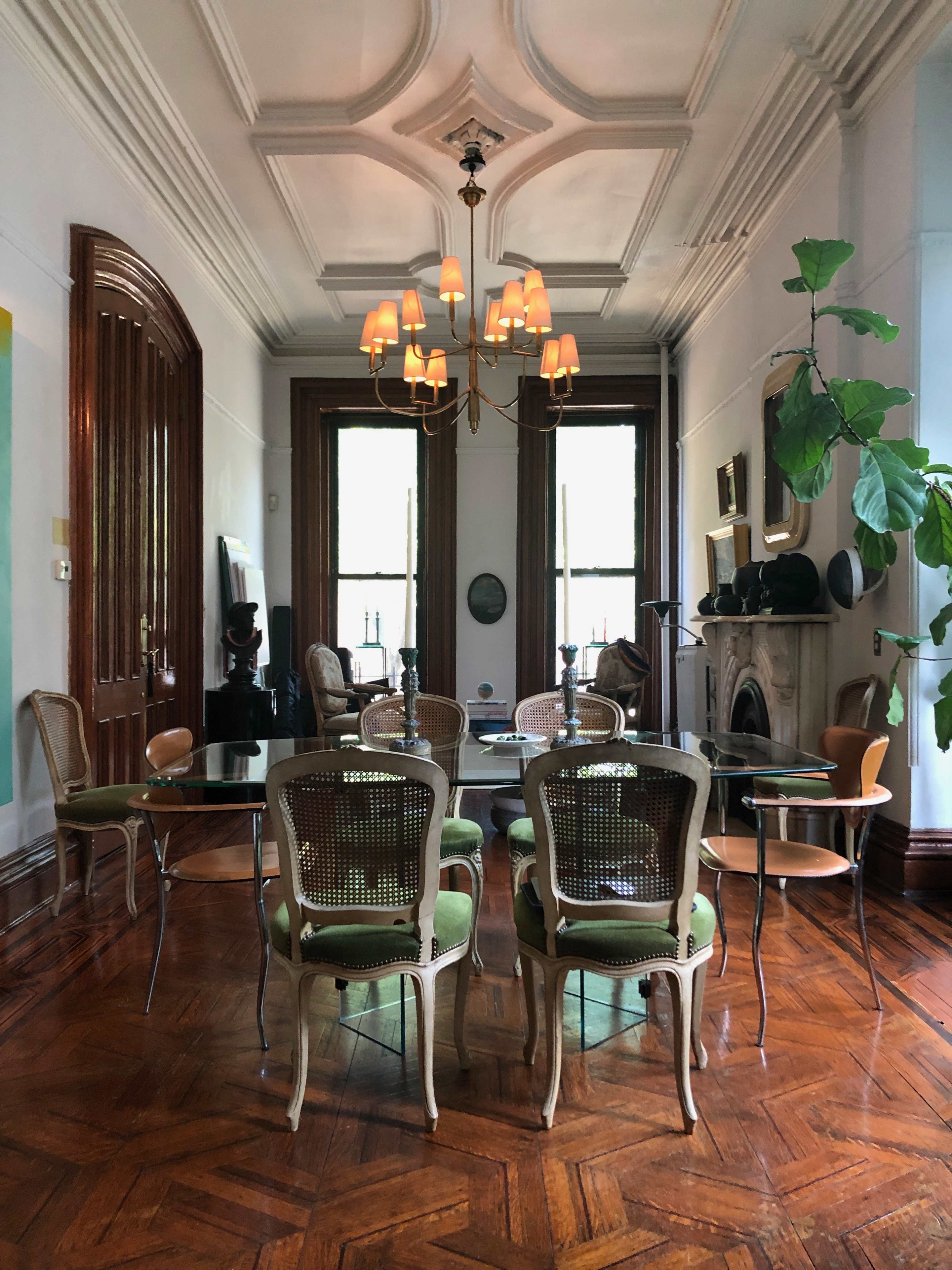 The image shows a spacious dining area with a wooden floor, a glass table surrounded by chairs, and large windows allowing natural light to enter.