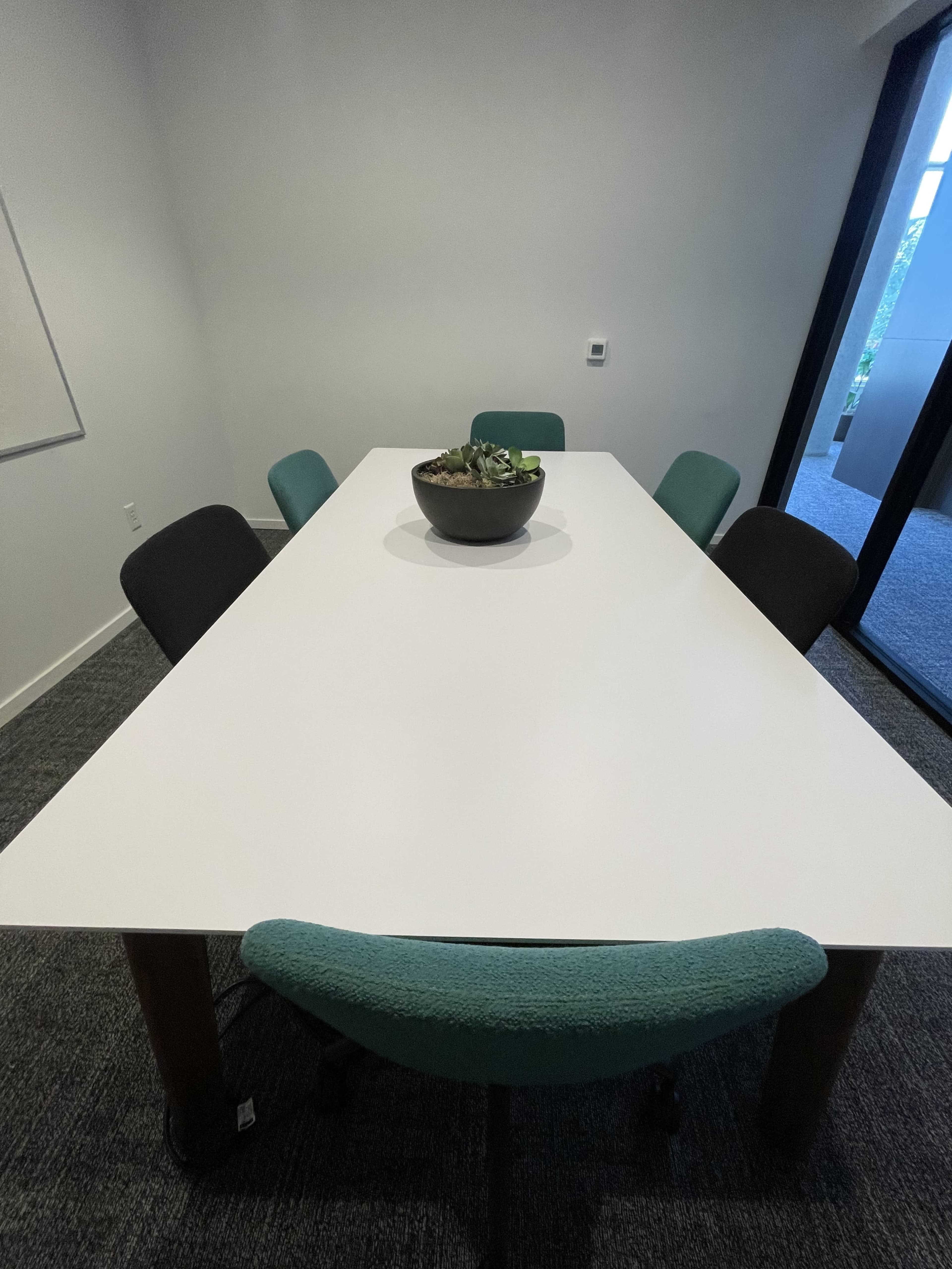 A large white table with a round pot of succulents is surrounded by four chairs in a well-lit meeting room.
