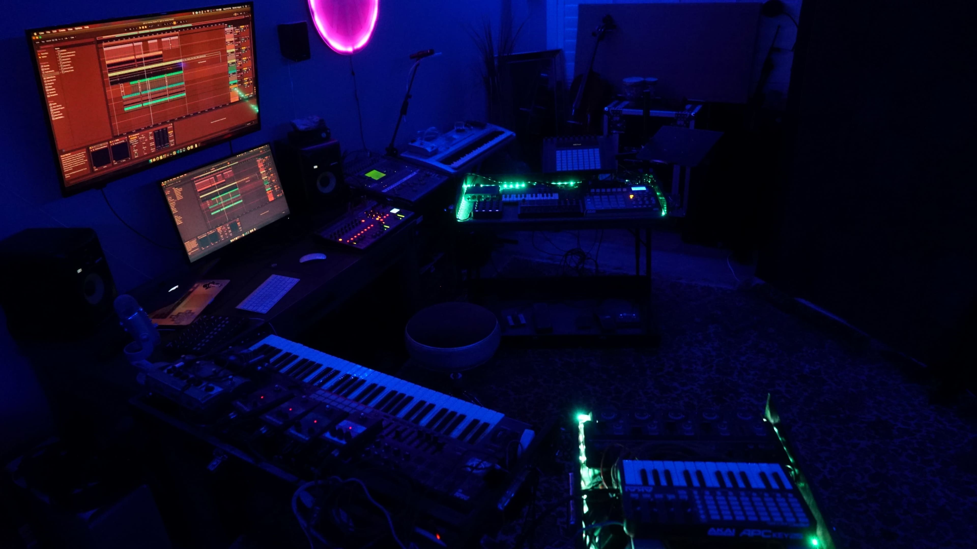 A music production studio is filled with various electronic instruments and illuminated equipment under blue lighting.