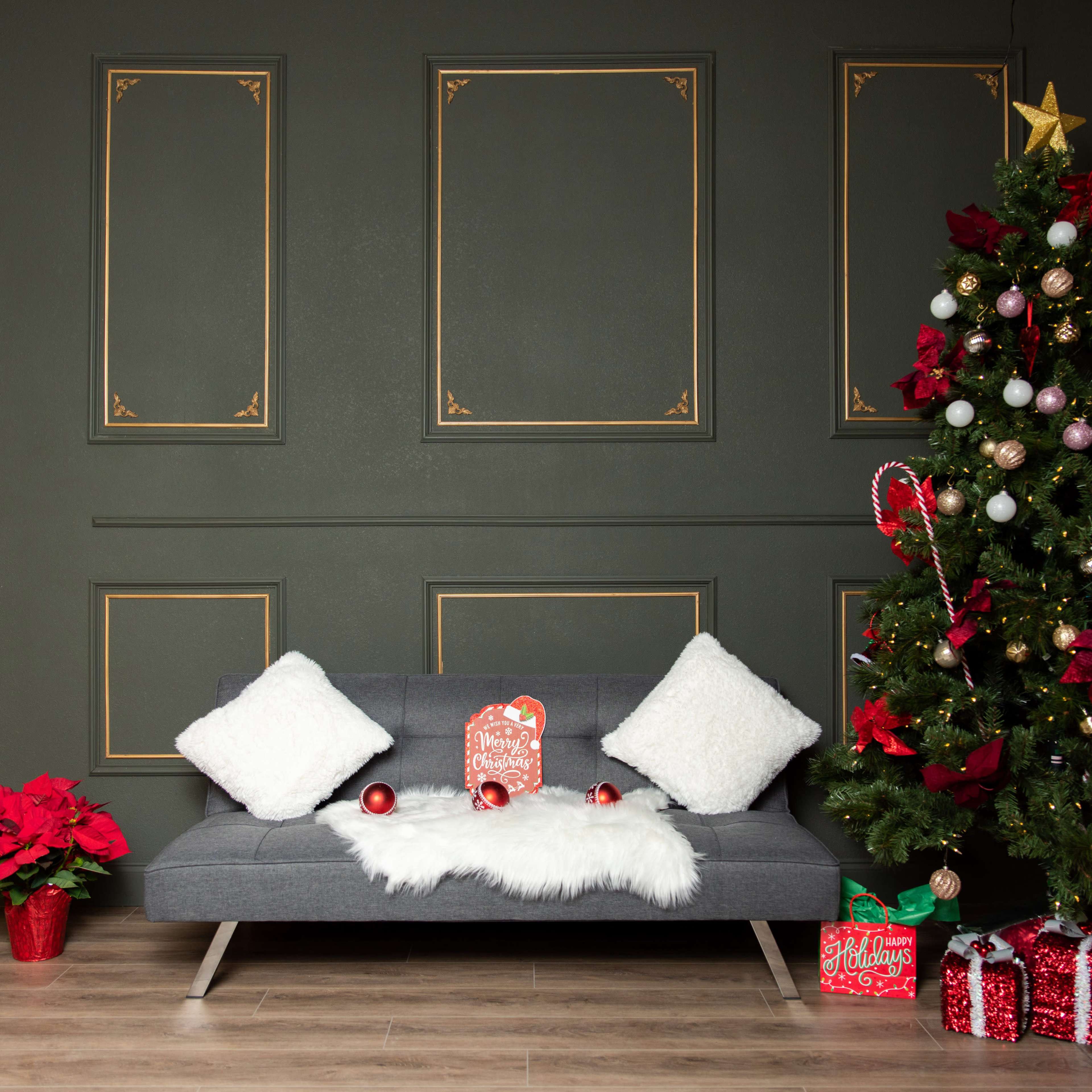 A cozy seating area features a gray couch adorned with white pillows and a fur throw, alongside a decorated Christmas tree and festive holiday decorations.