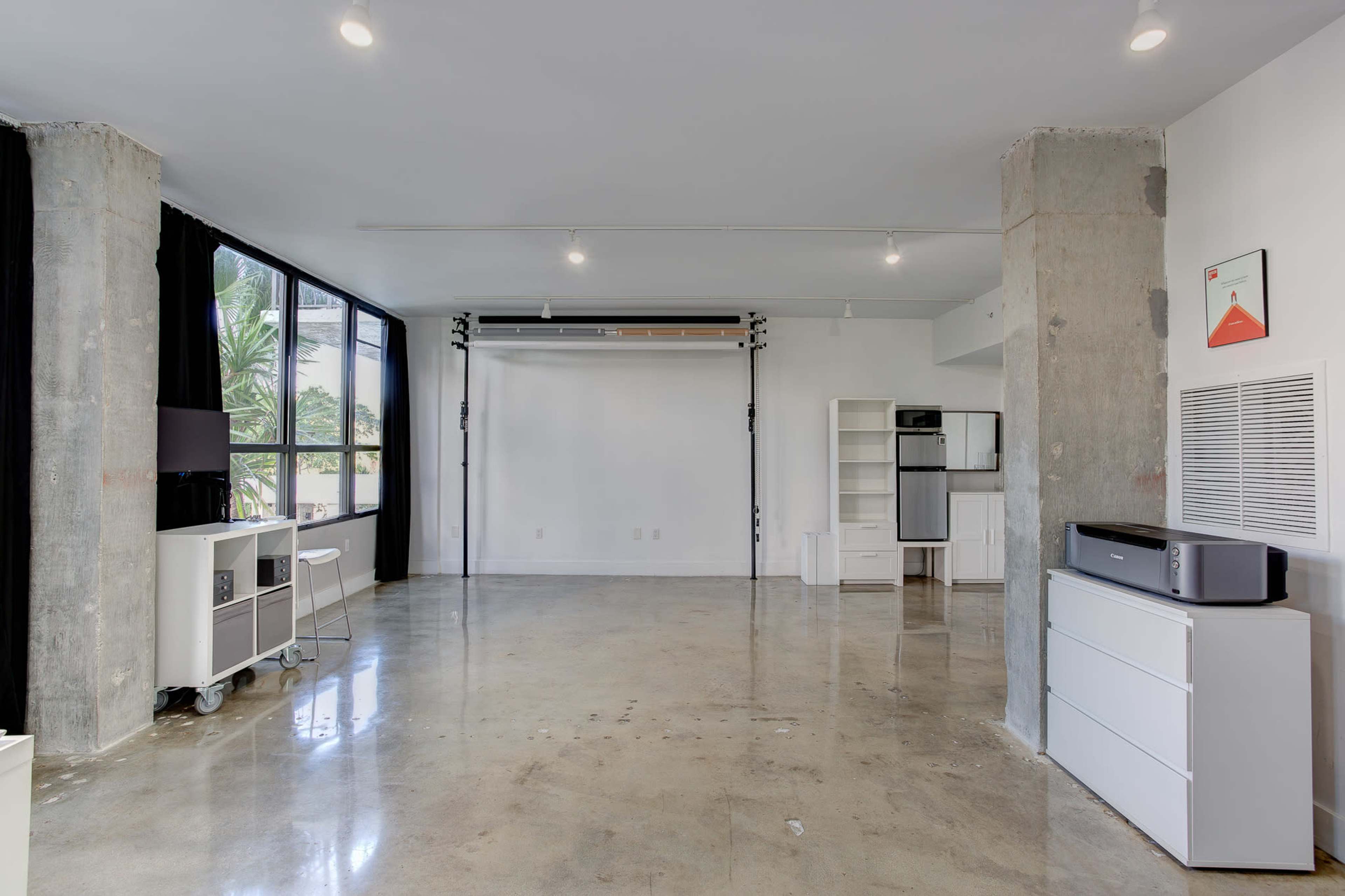 The room features a spacious, minimalist design with concrete pillars and large windows, offering ample natural light.