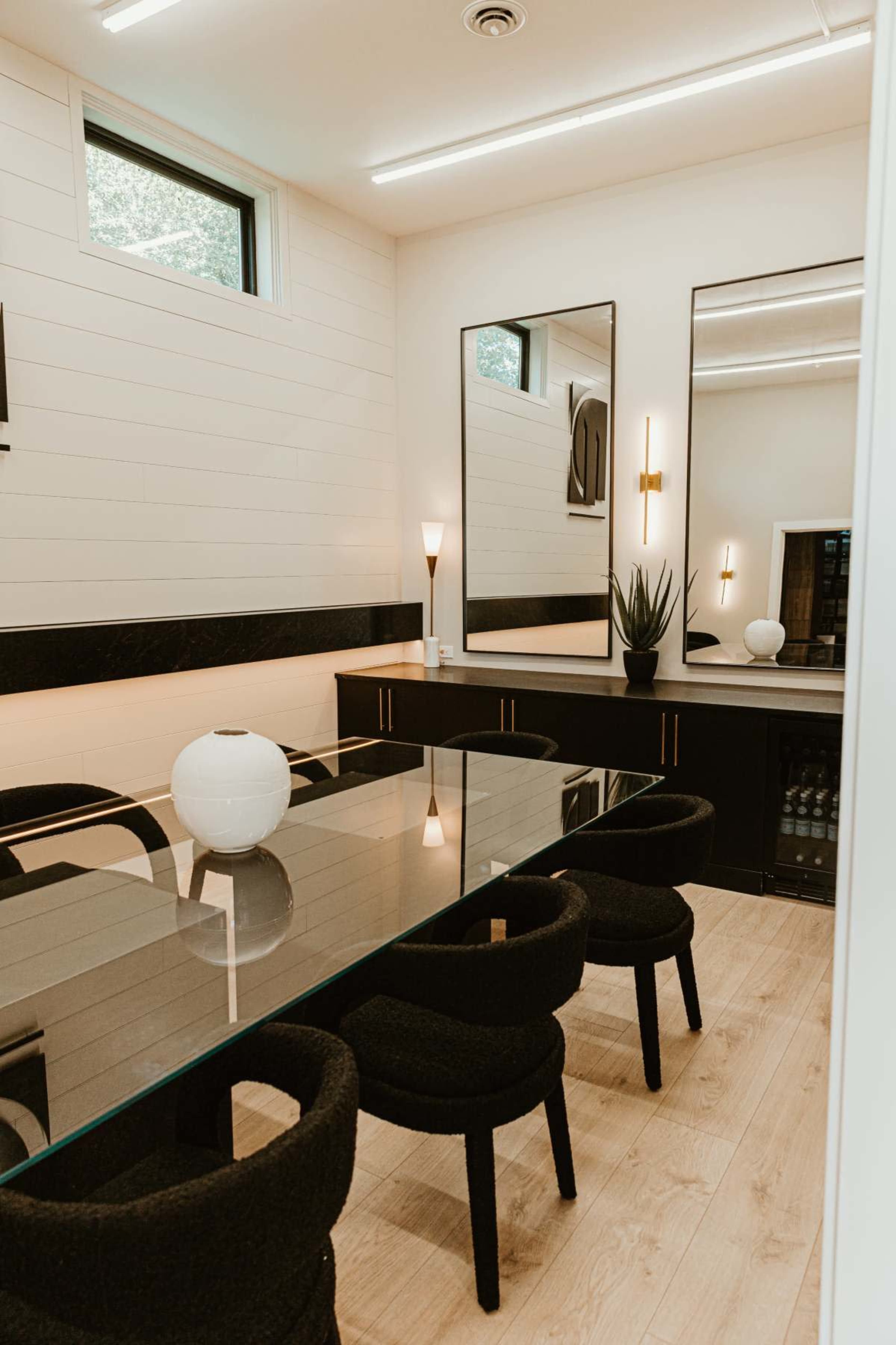 A sleek dining area features a glass table surrounded by black upholstered chairs, with two mirrors and modern decor on the walls.