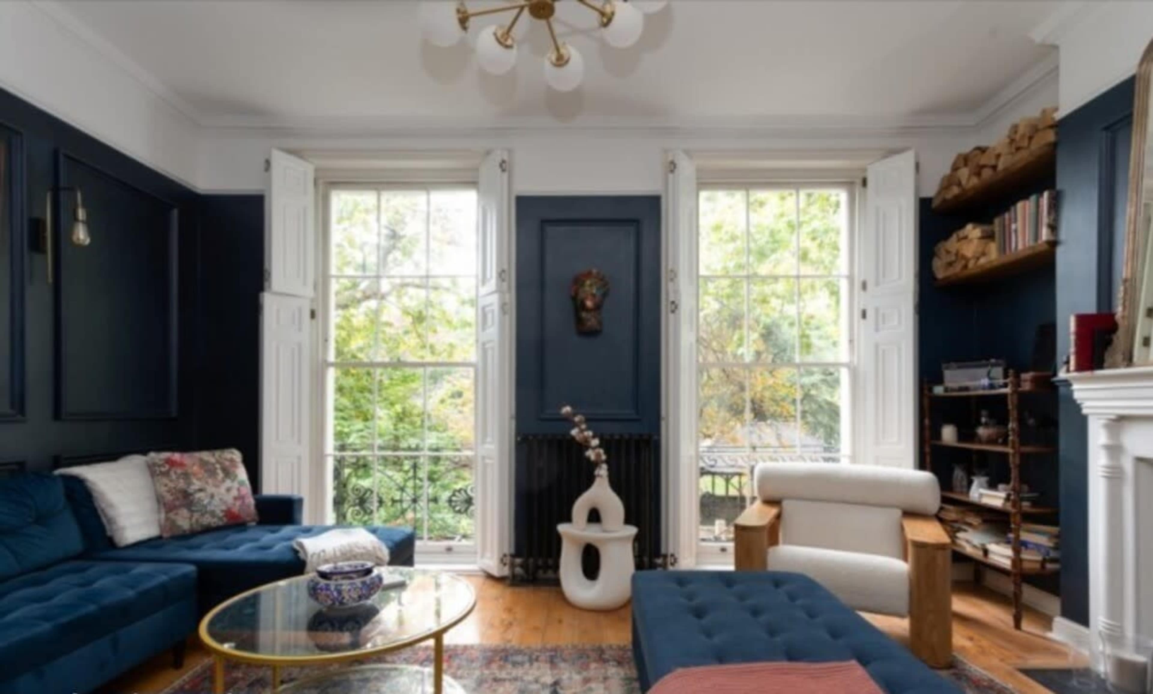 The room features a blue-walled living area with large windows, a coffee table, and a mix of modern and traditional furniture.