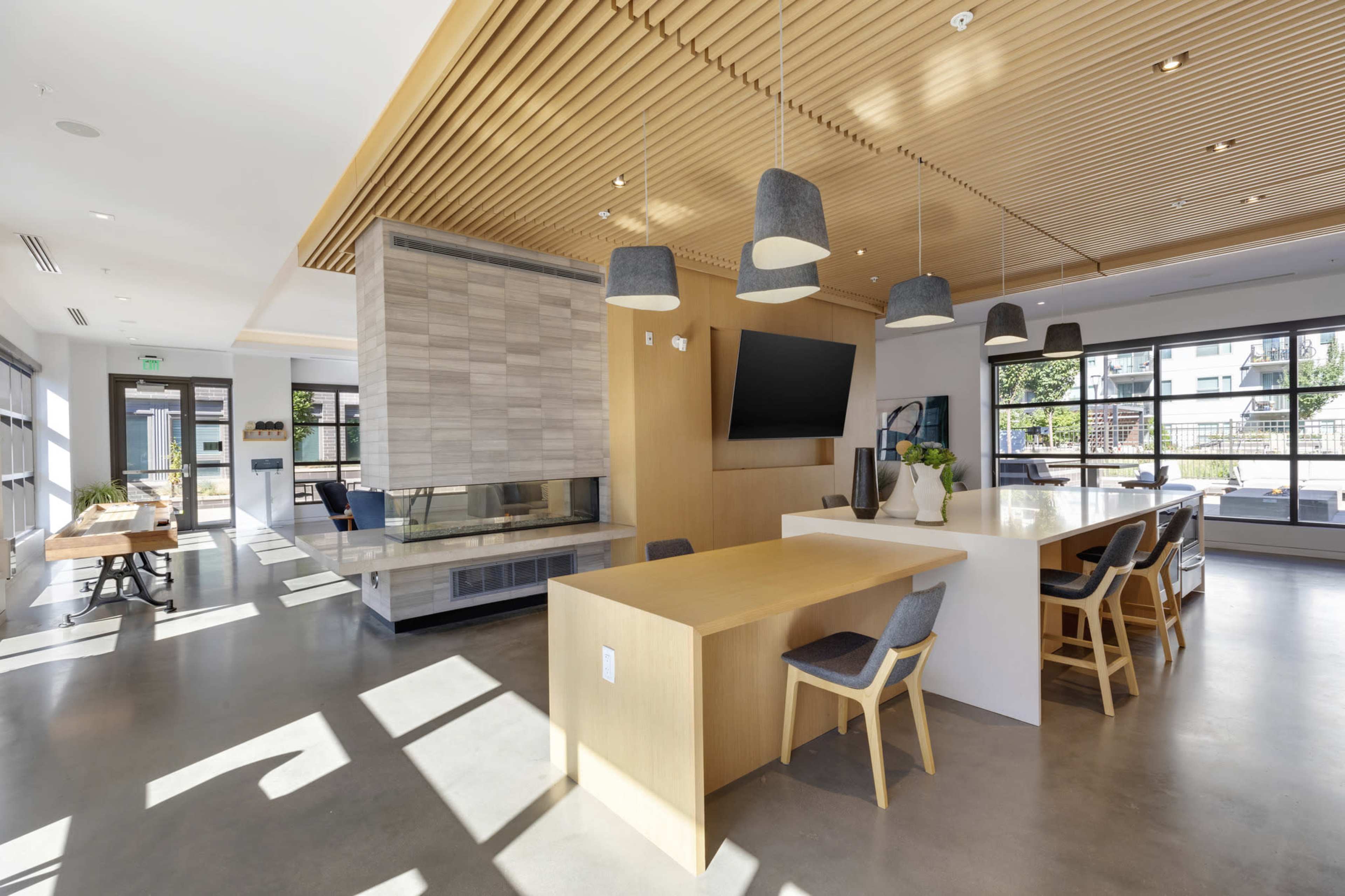 A modern interior space featuring a kitchen island, dining area, and a large window with natural light, highlighted by wooden ceiling panels and minimalist decor.