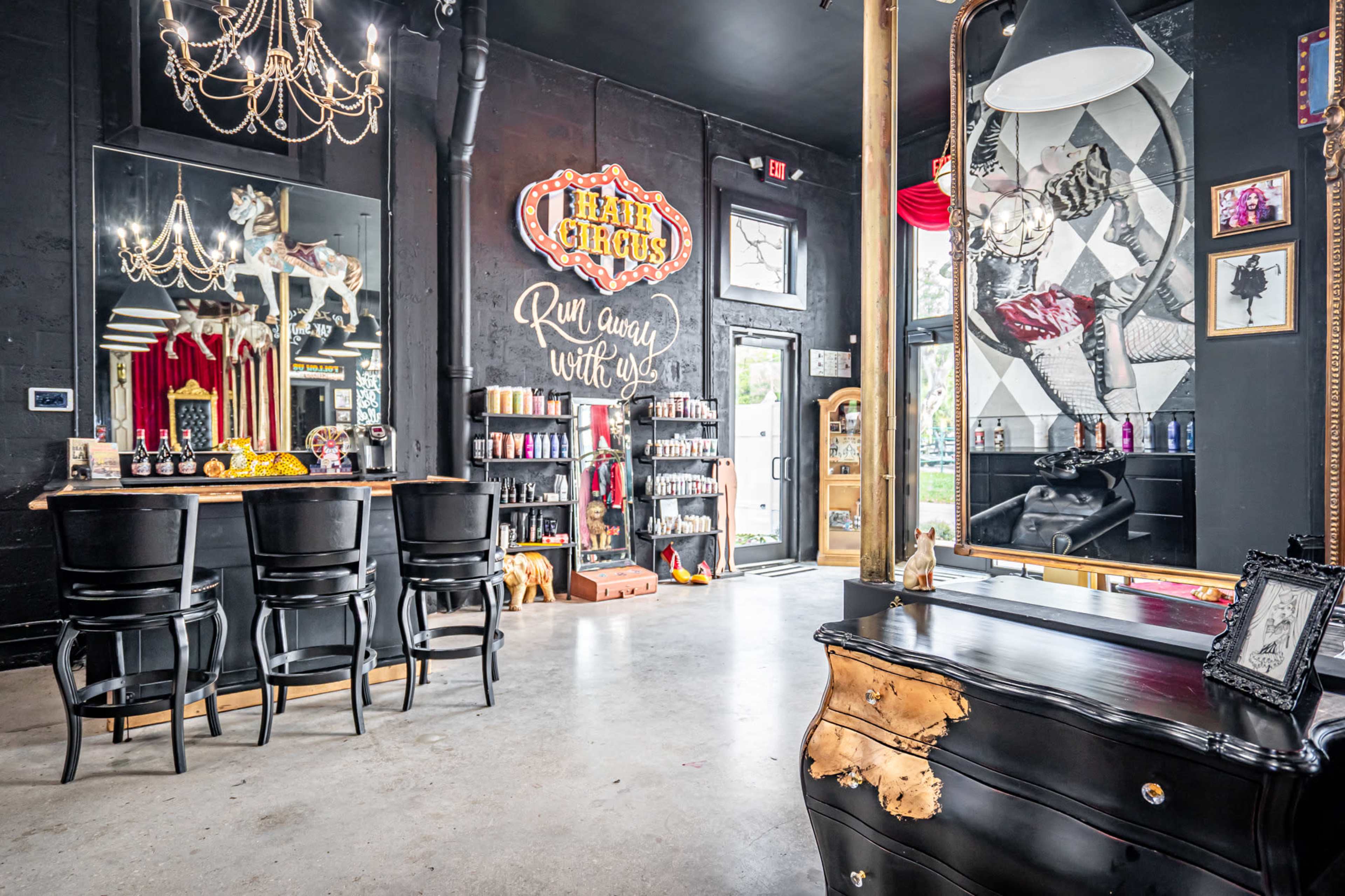 A stylish salon interior featuring a bar counter, a large mirror, and decorative elements like a chandelier and a vintage sign.