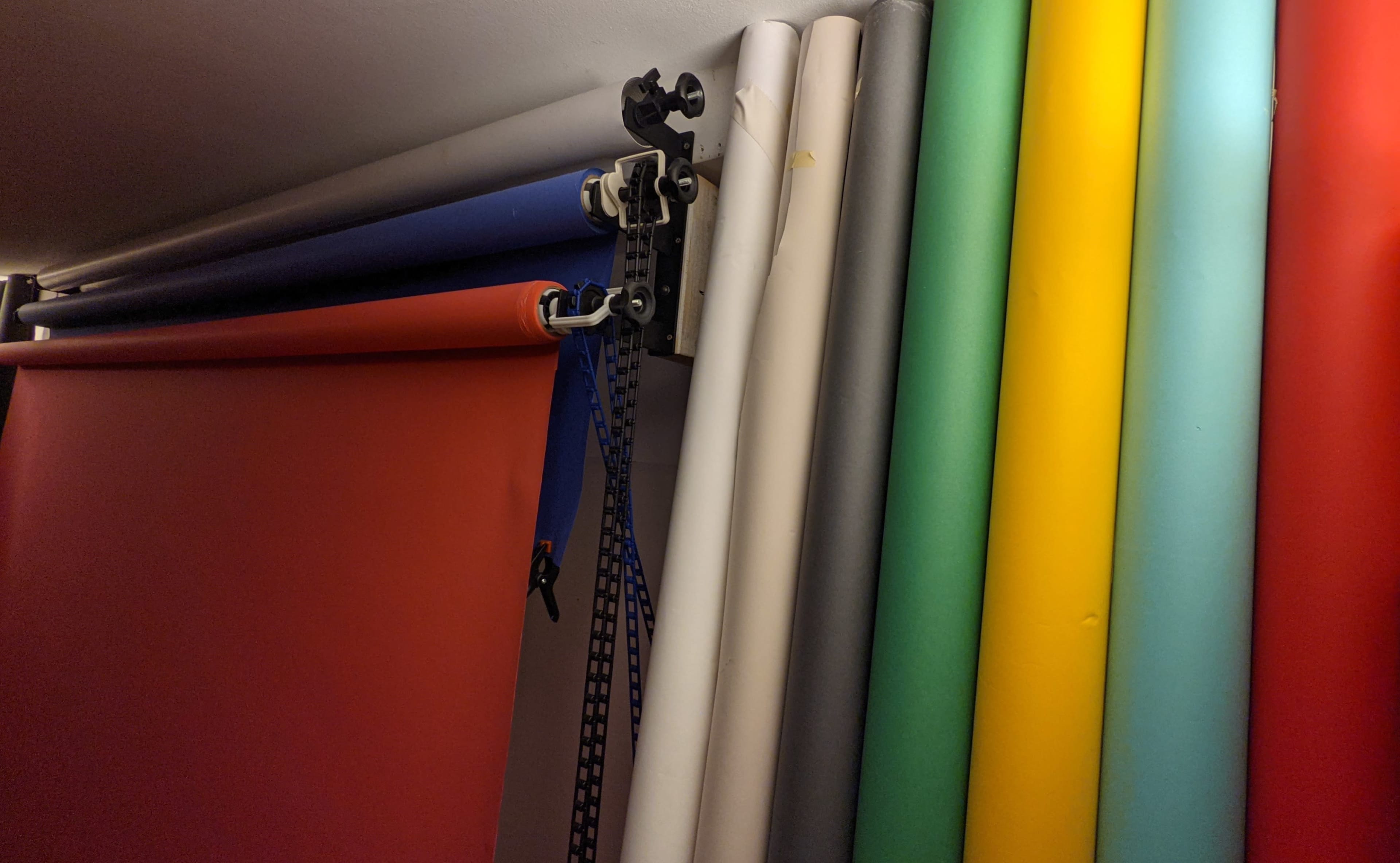 A stack of colorful photographic backdrops rolled and hanging on a support, with a blue strap visible on the side.