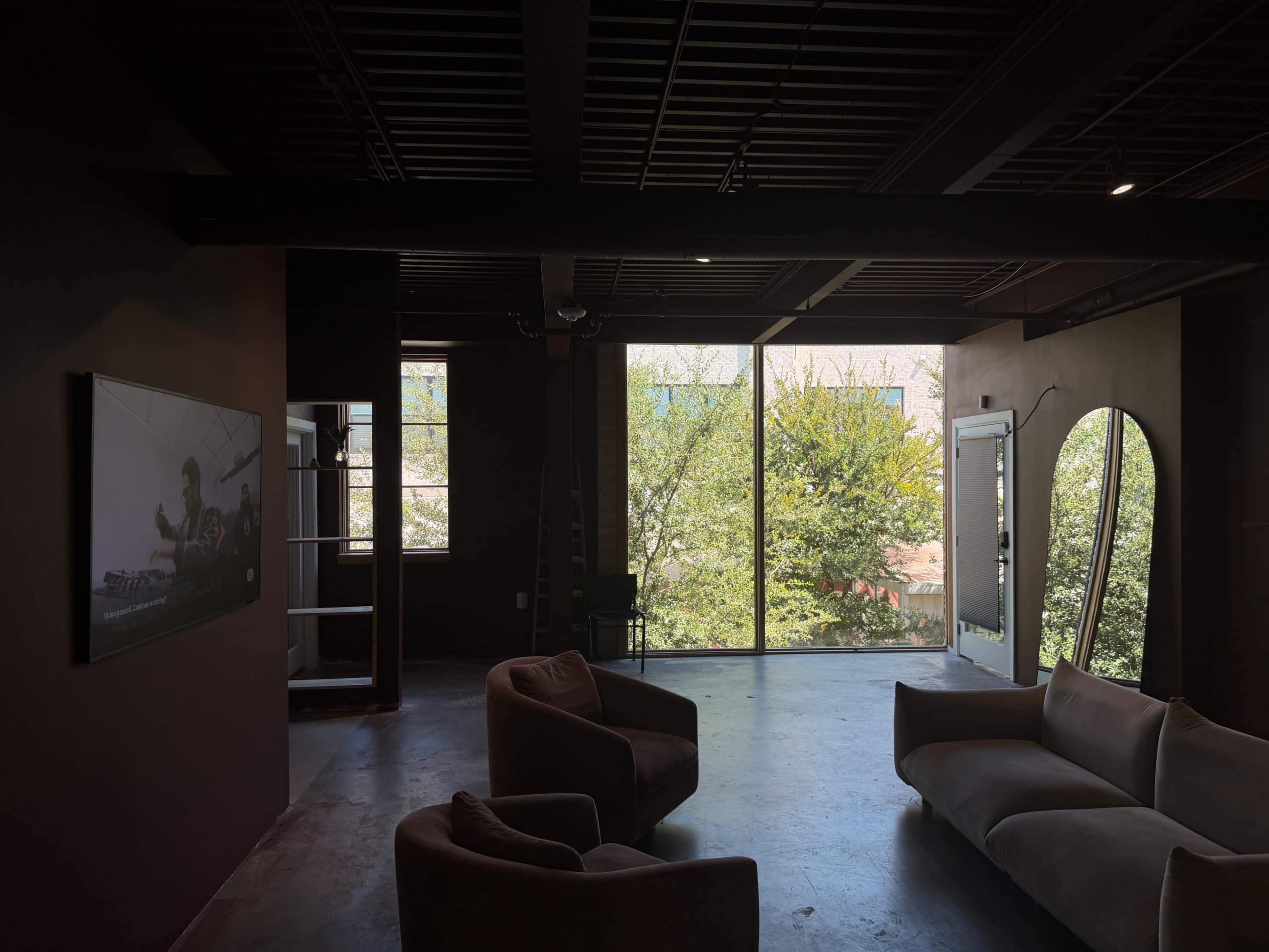 A spacious room features two armchairs and a sofa, with large windows displaying green trees outside.
