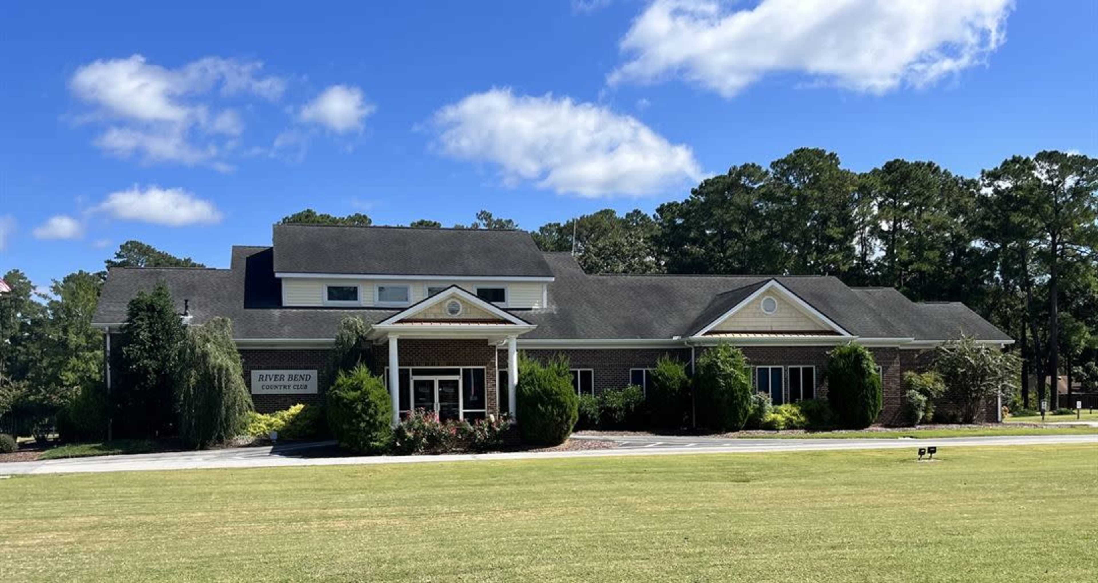 A large brick community center surrounded by a well-maintained lawn and trees under a blue sky.