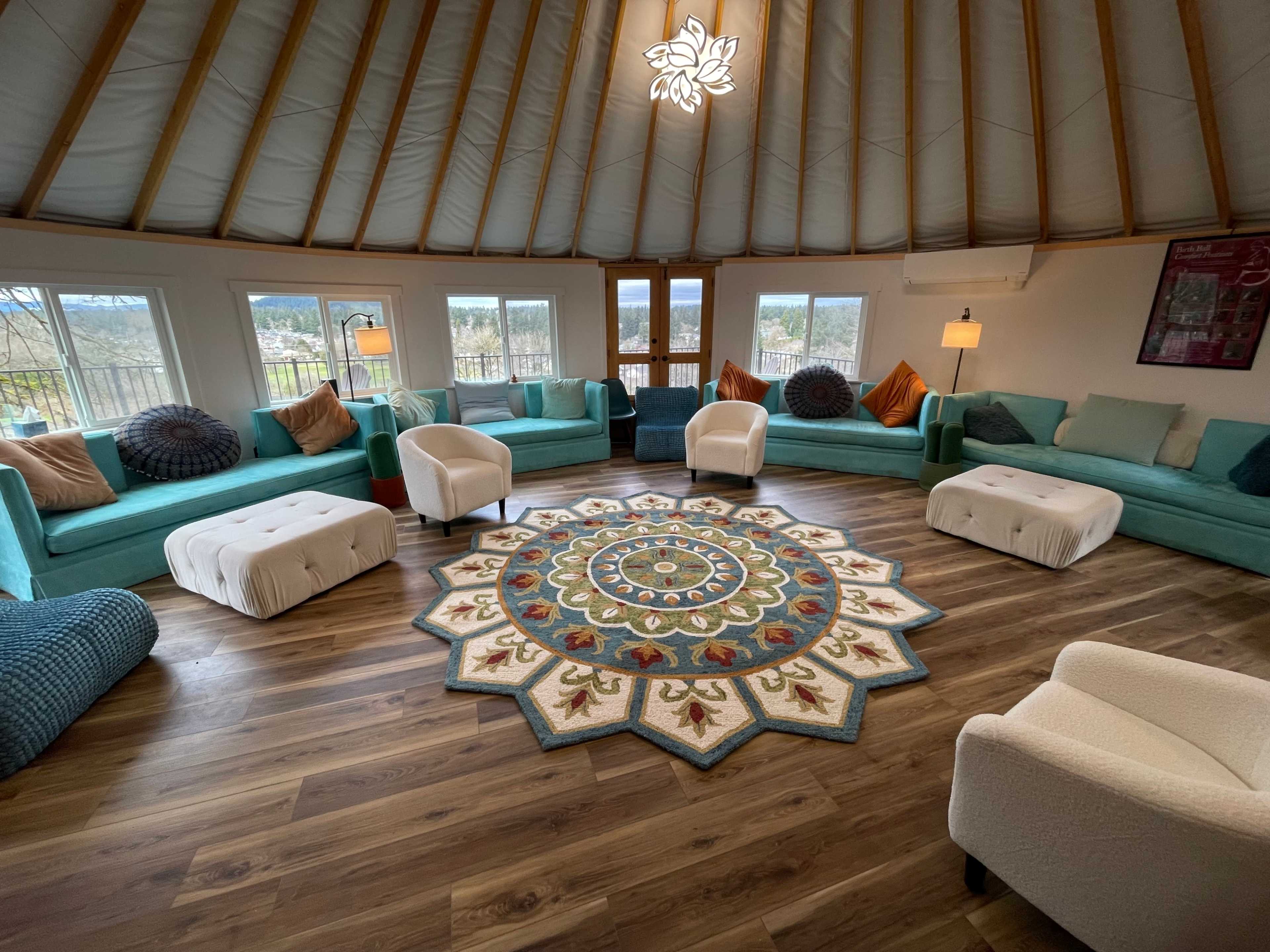 A round, airy lounge space with turquoise sofas, white armchairs, and a large, decorative area rug at the center.