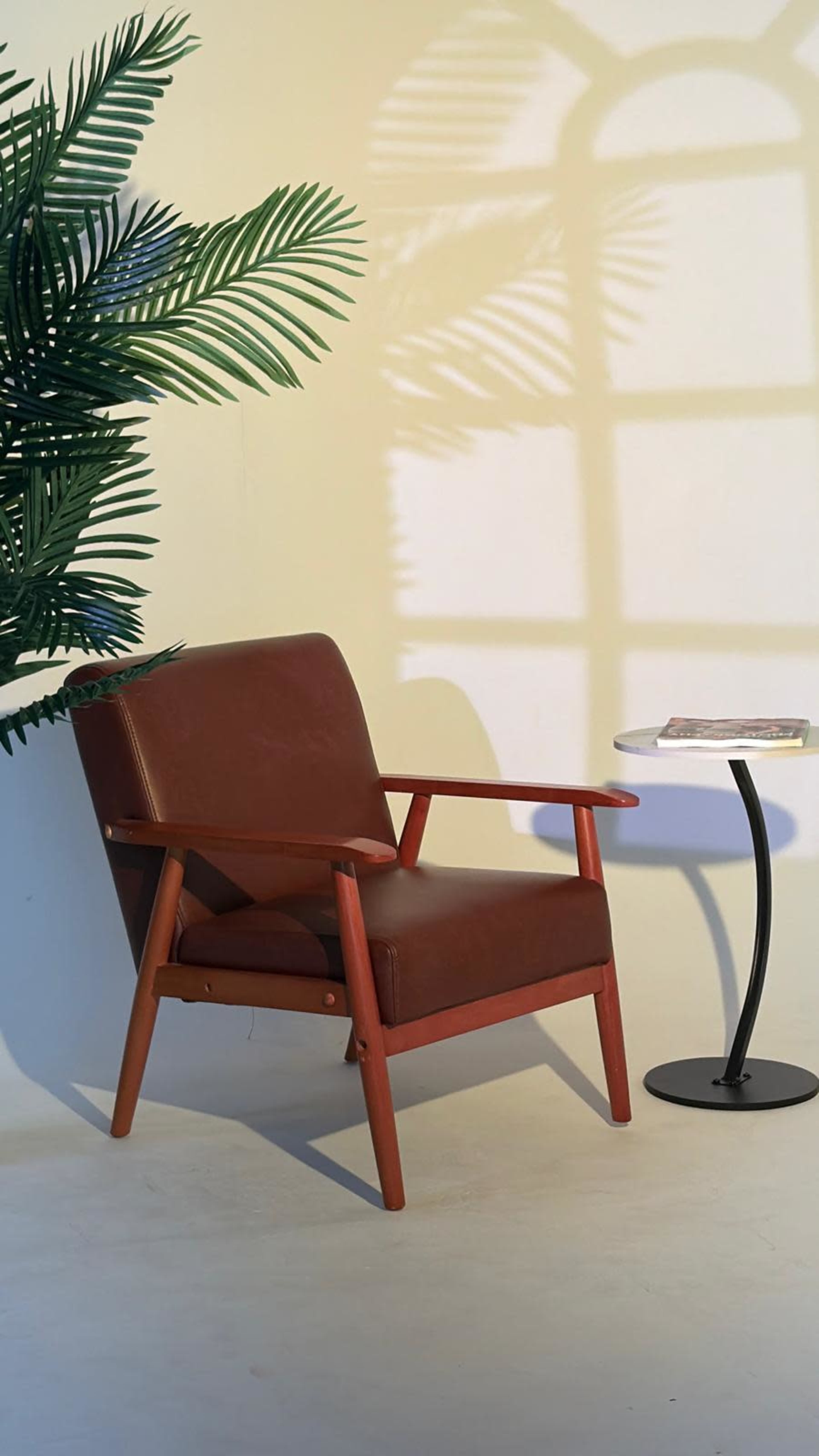 A brown leather armchair sits beside a small black table, with a shadow of a window pattern cast on the wall.