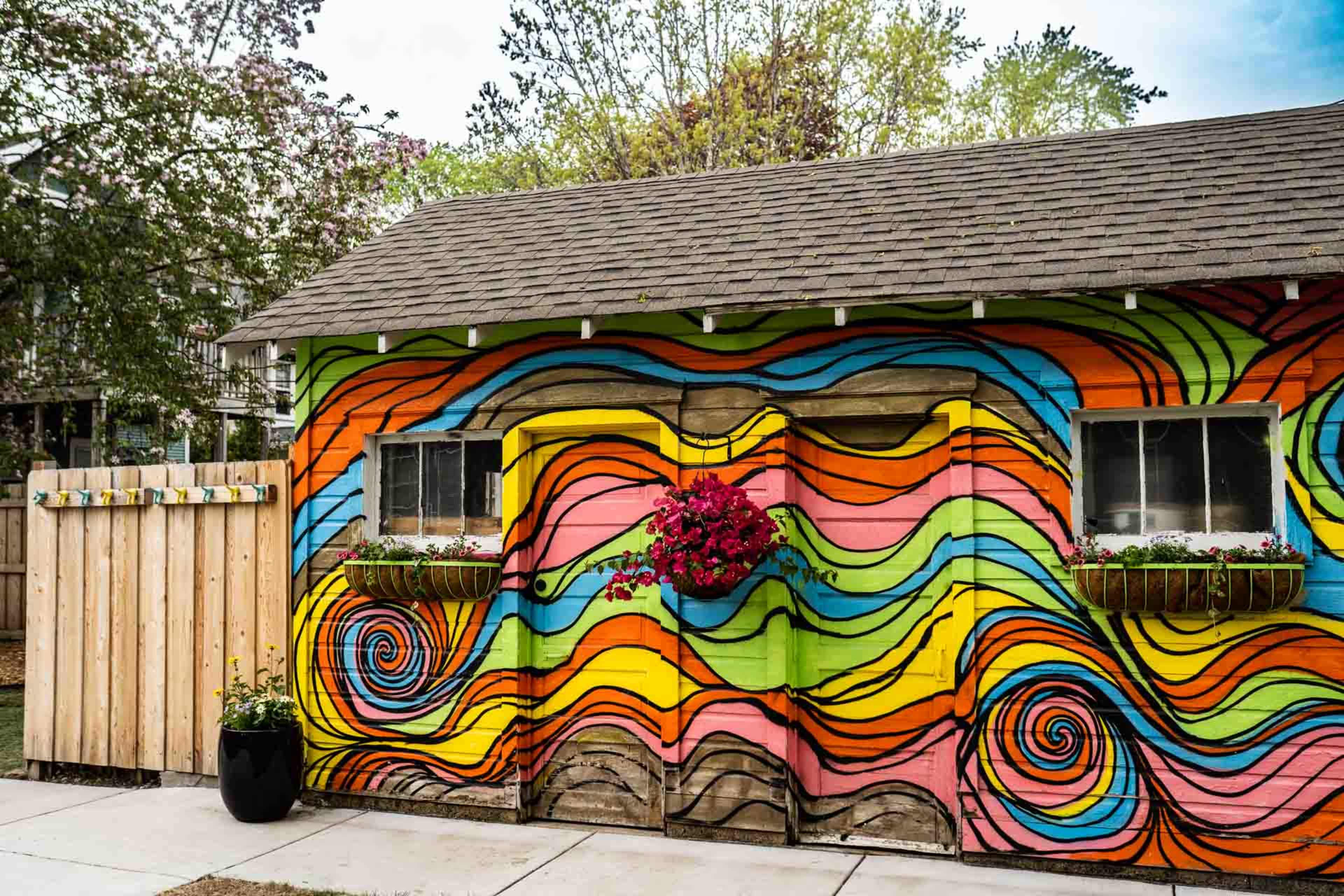 A colorful mural with swirling patterns covers the exterior of a small shed, which features two windows adorned with flower boxes.