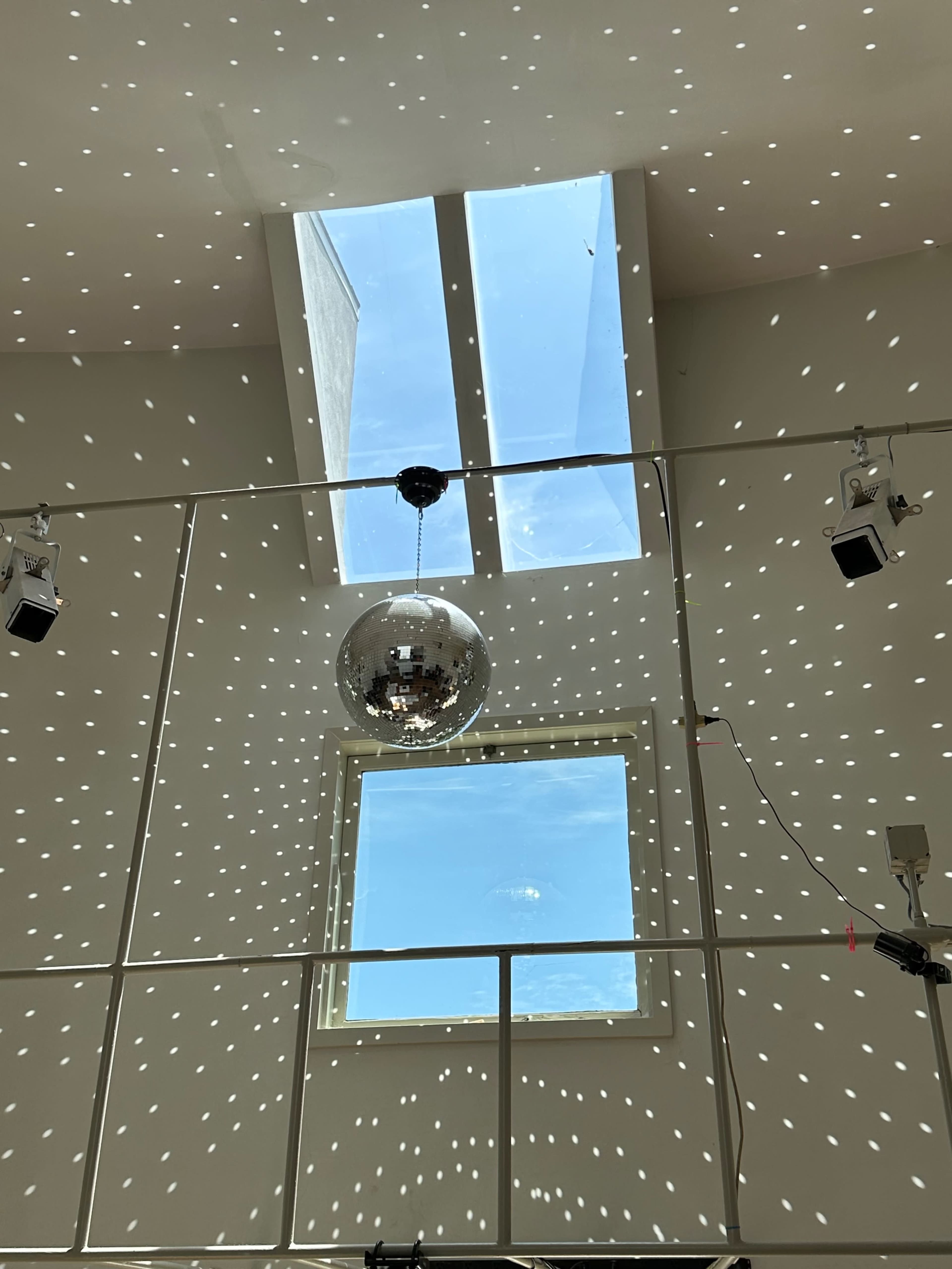 A disco ball hangs from a ceiling while sunlight streams through a skylight, creating scattered light patterns on the walls.