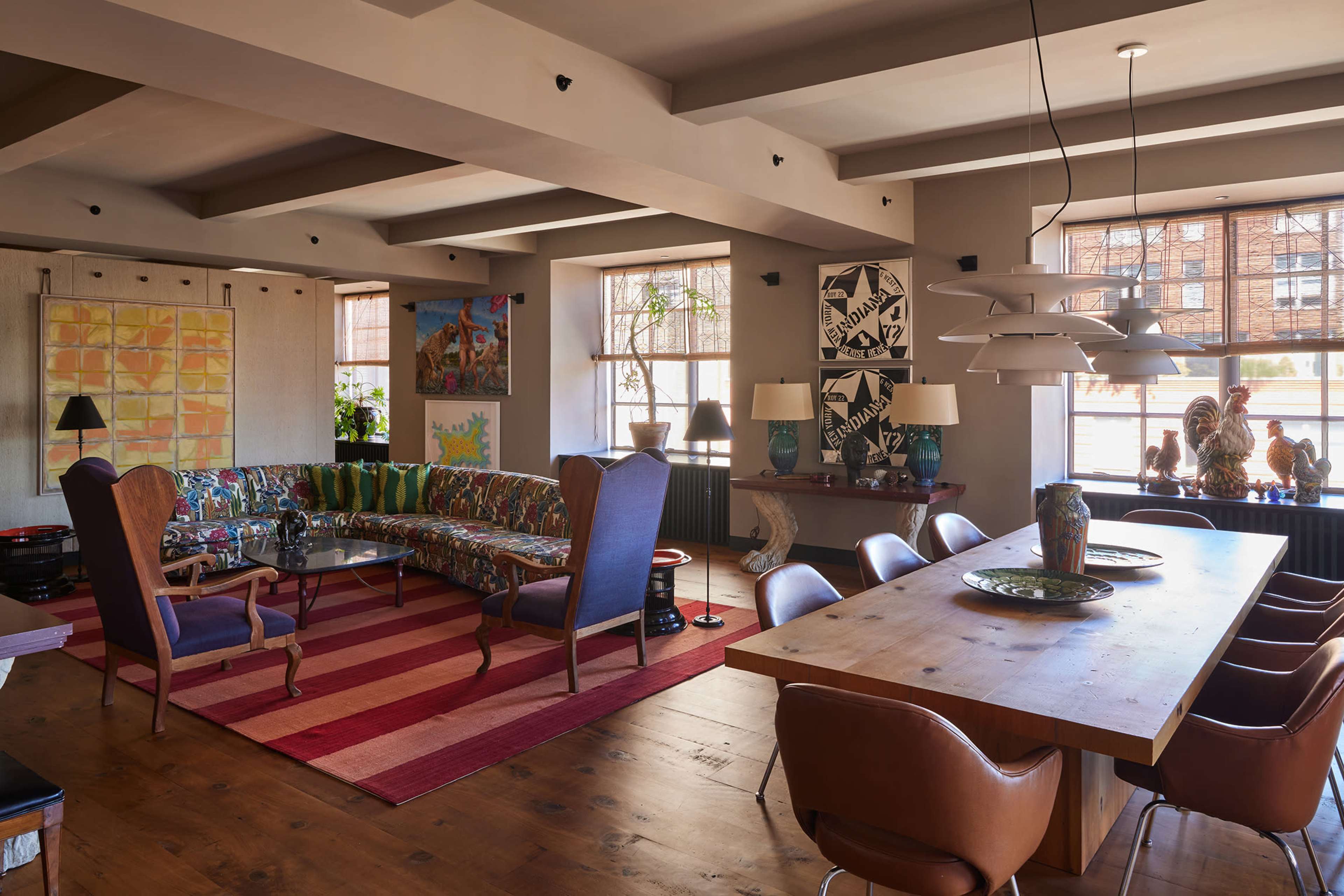 The image shows a spacious living area with a colorful patterned sofa, a wooden dining table, and various artworks on the walls.