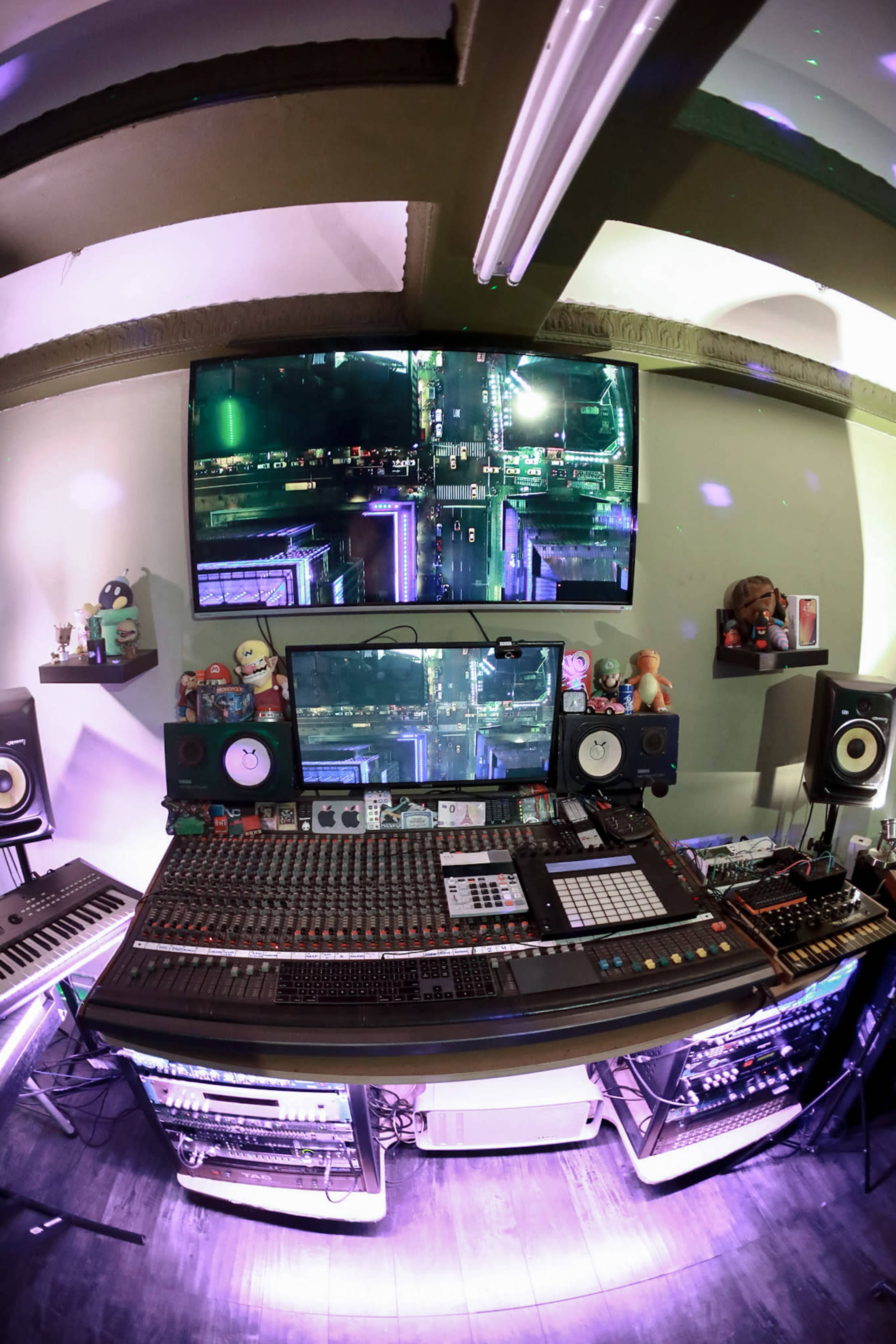 The image shows a music production studio equipped with various sound mixers, speakers, and multiple screens displaying visuals.