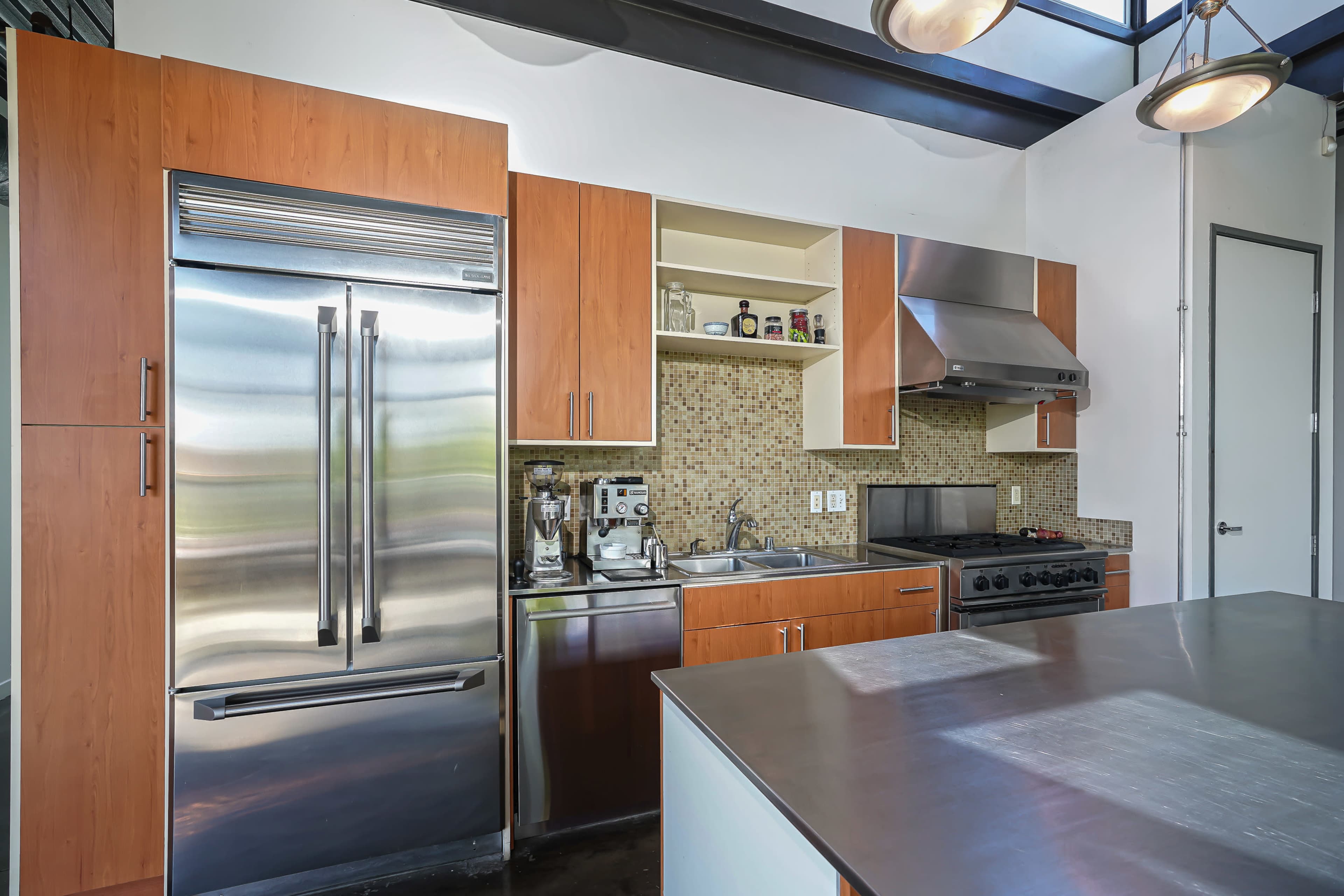 The image shows a modern kitchen featuring stainless steel appliances, wooden cabinetry, and a countertop with a muted color palette.