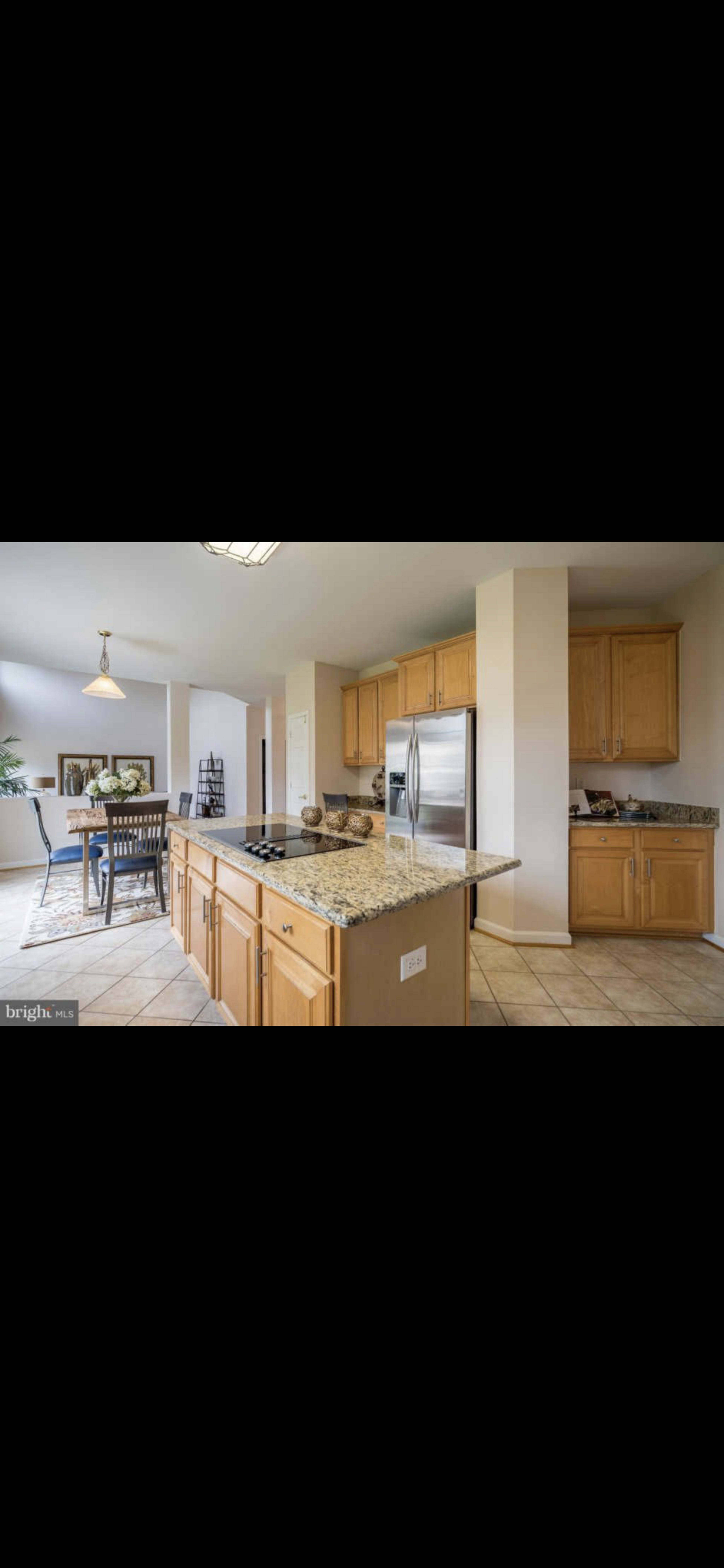 A modern kitchen features wooden cabinets, a granite countertop with a stove, and stainless steel appliances, adjacent to a dining area.