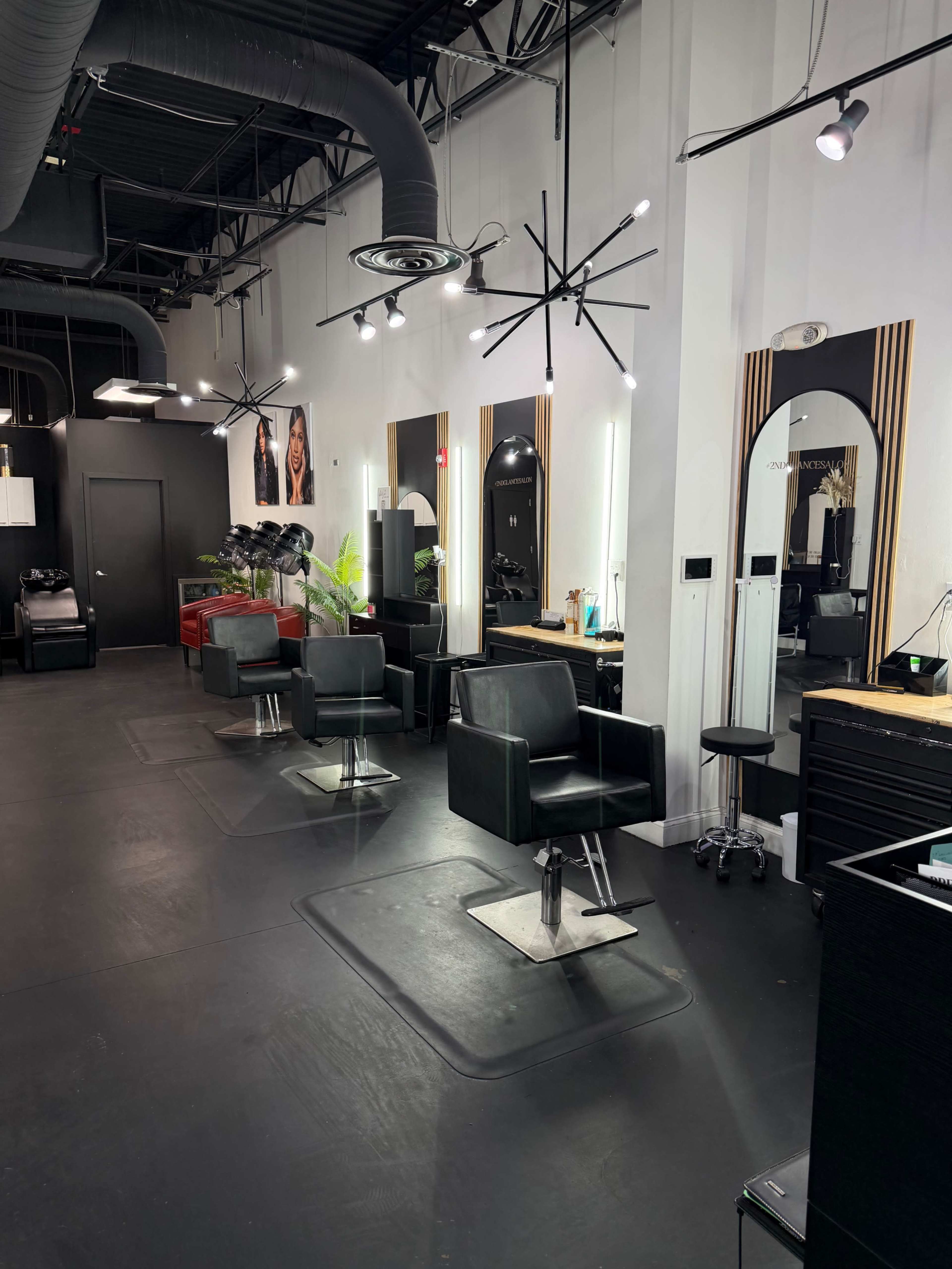 The image shows a modern hair salon with black styling chairs, mirrors, and a sleek interior design featuring overhead lighting and minimalistic decor.