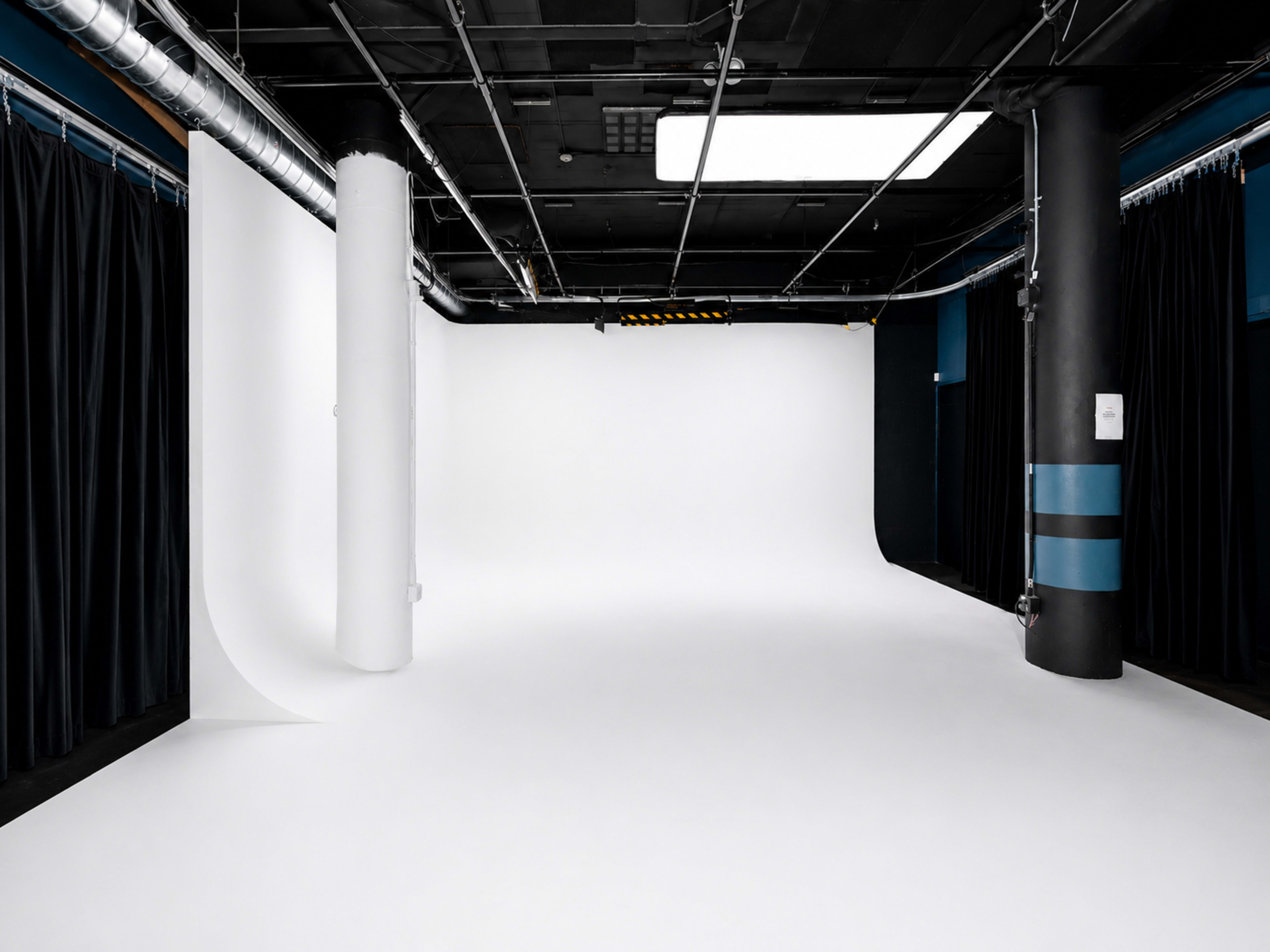 The image shows a spacious photography studio with a white backdrop and black curtains on the sides.