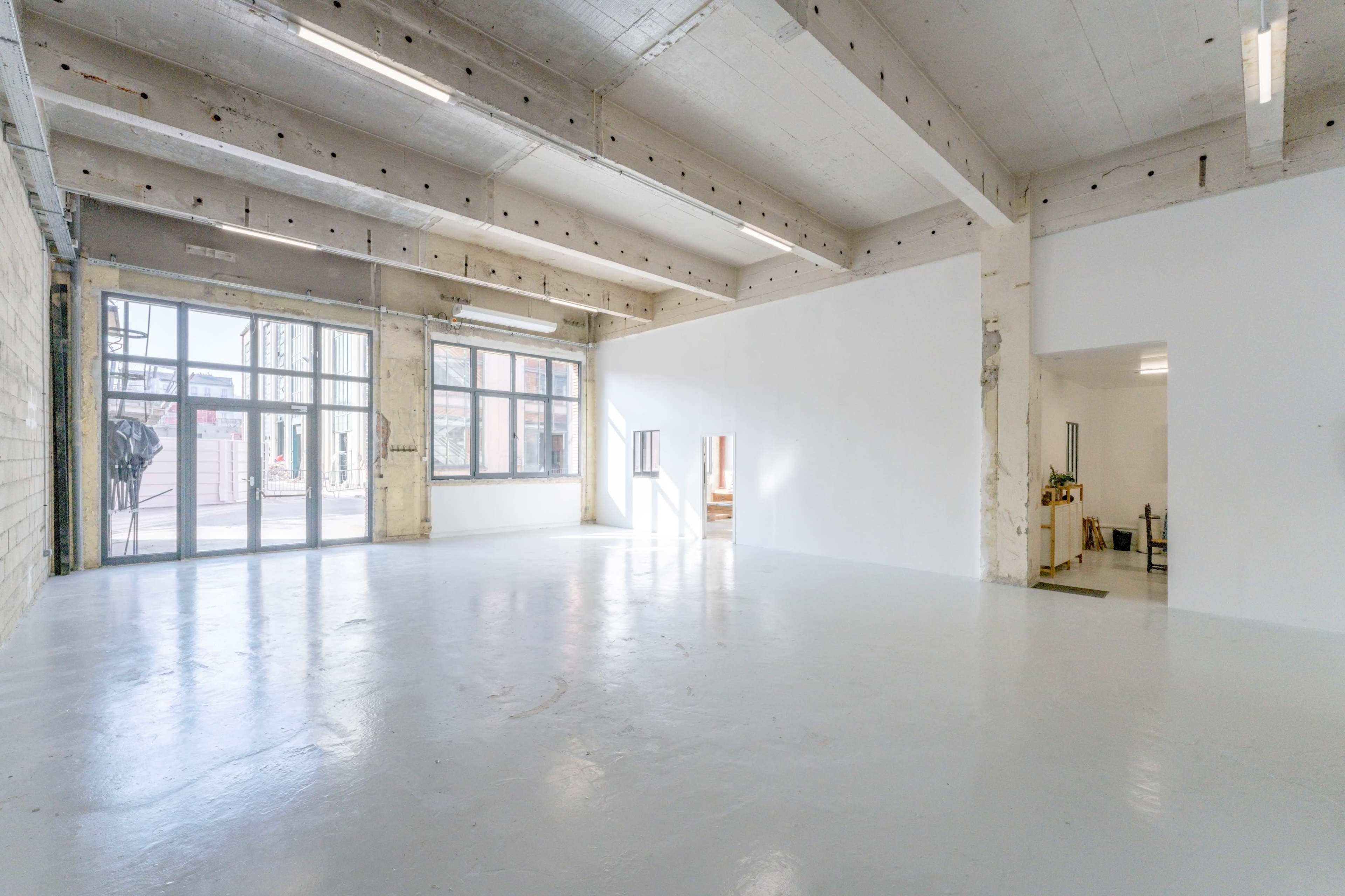 A spacious industrial-style room with large windows and polished white flooring.
