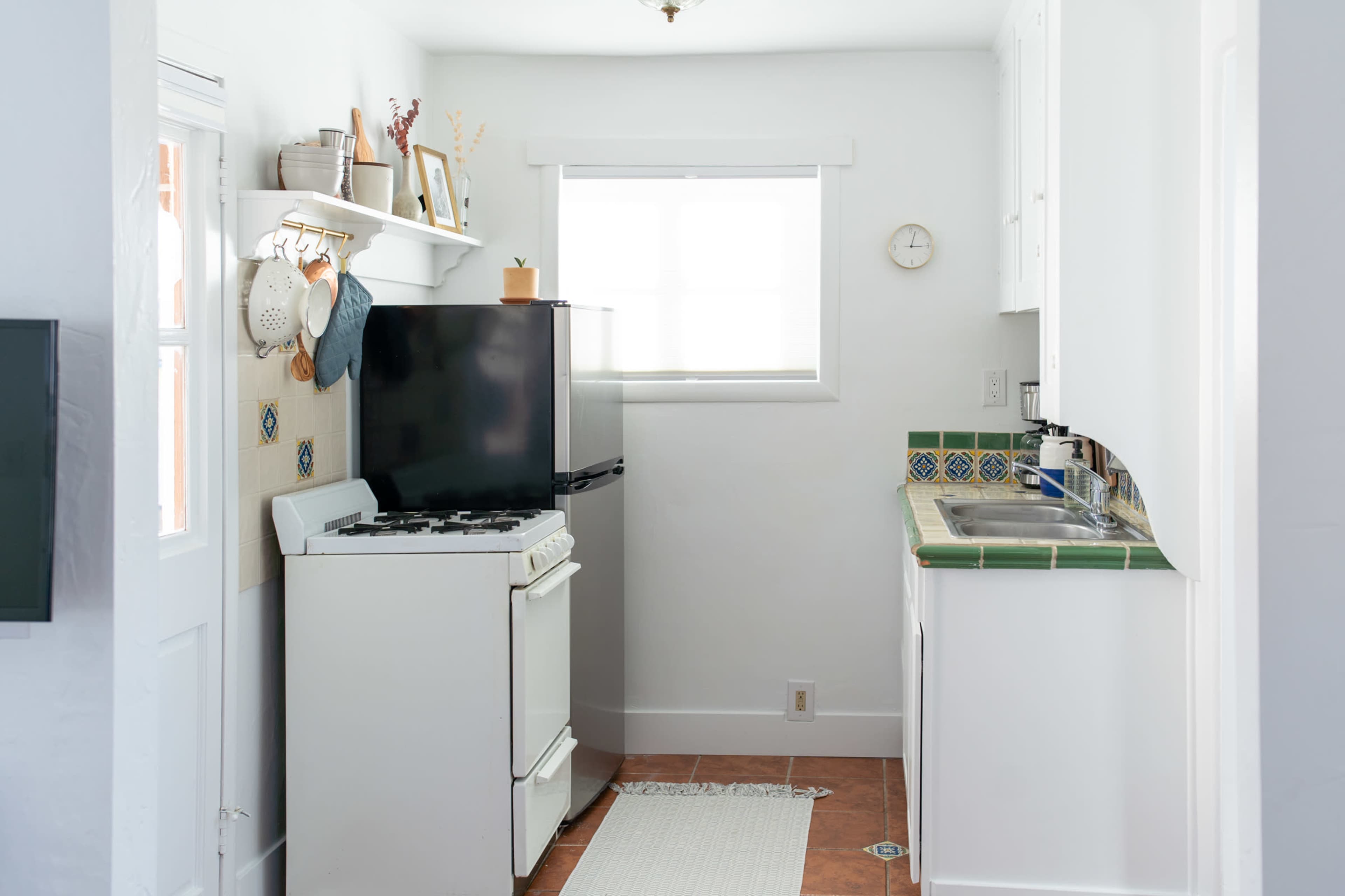 A compact kitchen featuring a black refrigerator, a white stove, a sink, and light-colored cabinetry against a tiled backsplash.