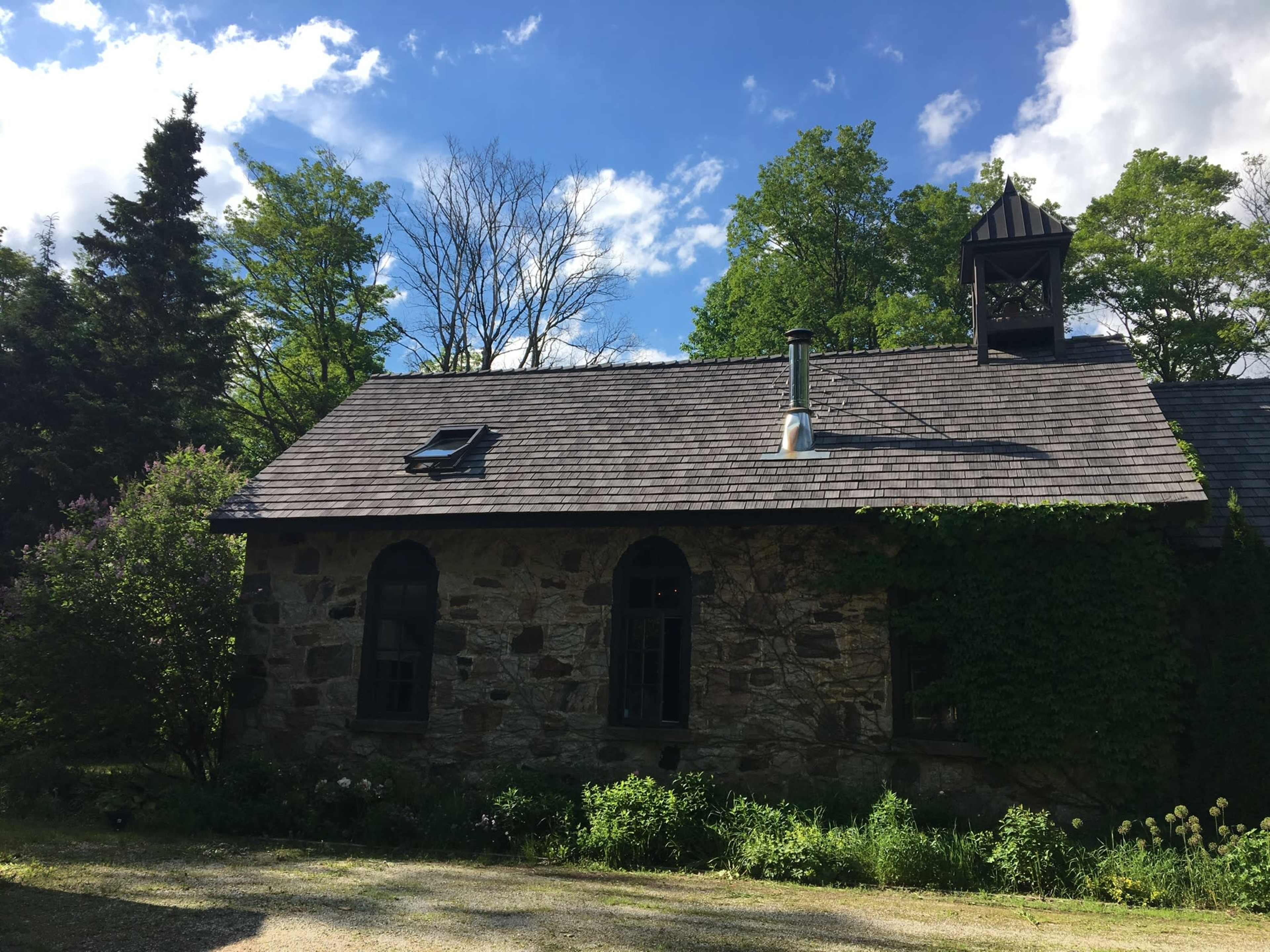 A stone house with a chimney and a skylight is surrounded by trees and greenery.