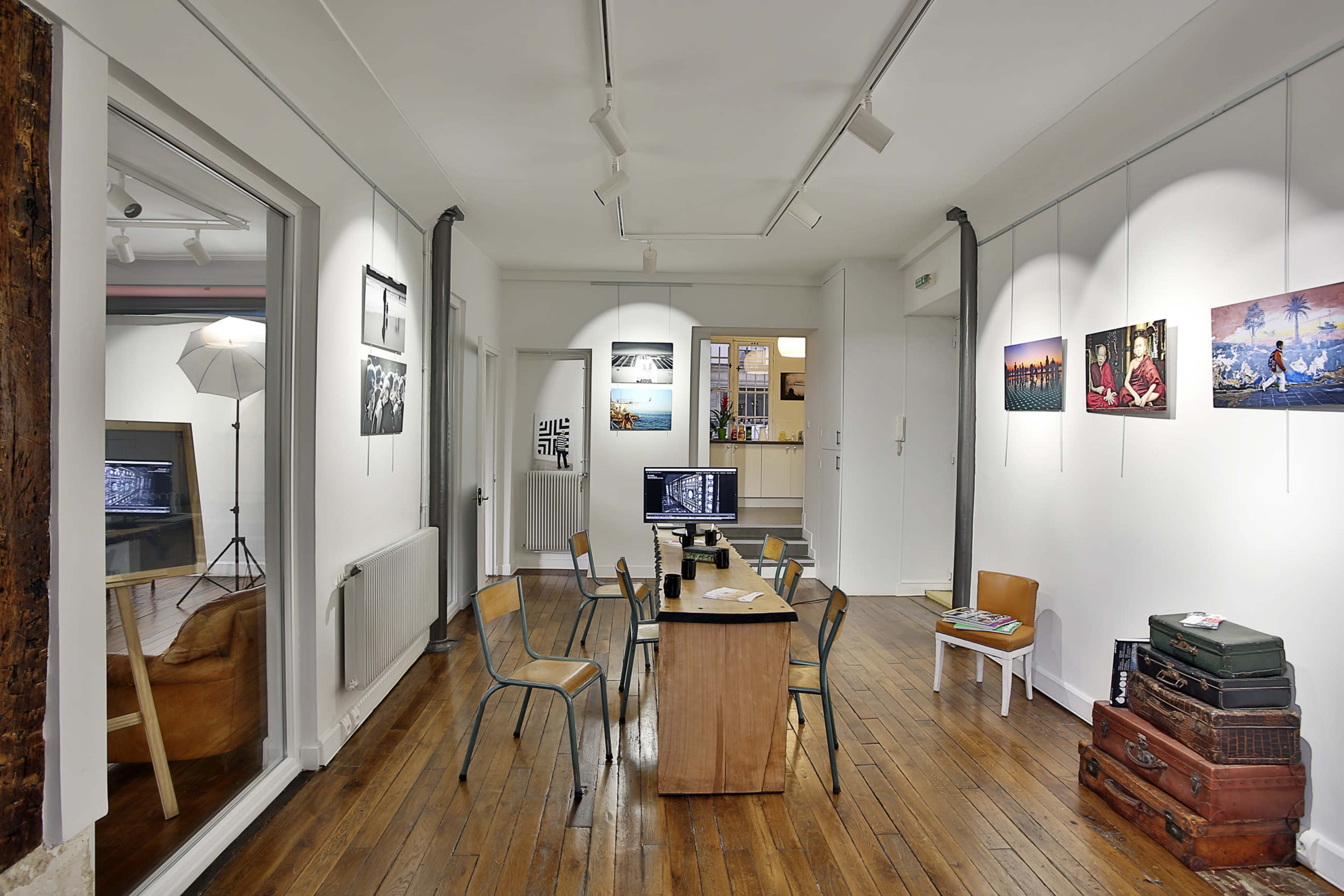 A modern art gallery features wooden flooring, simple furniture, and photographs displayed on the walls.