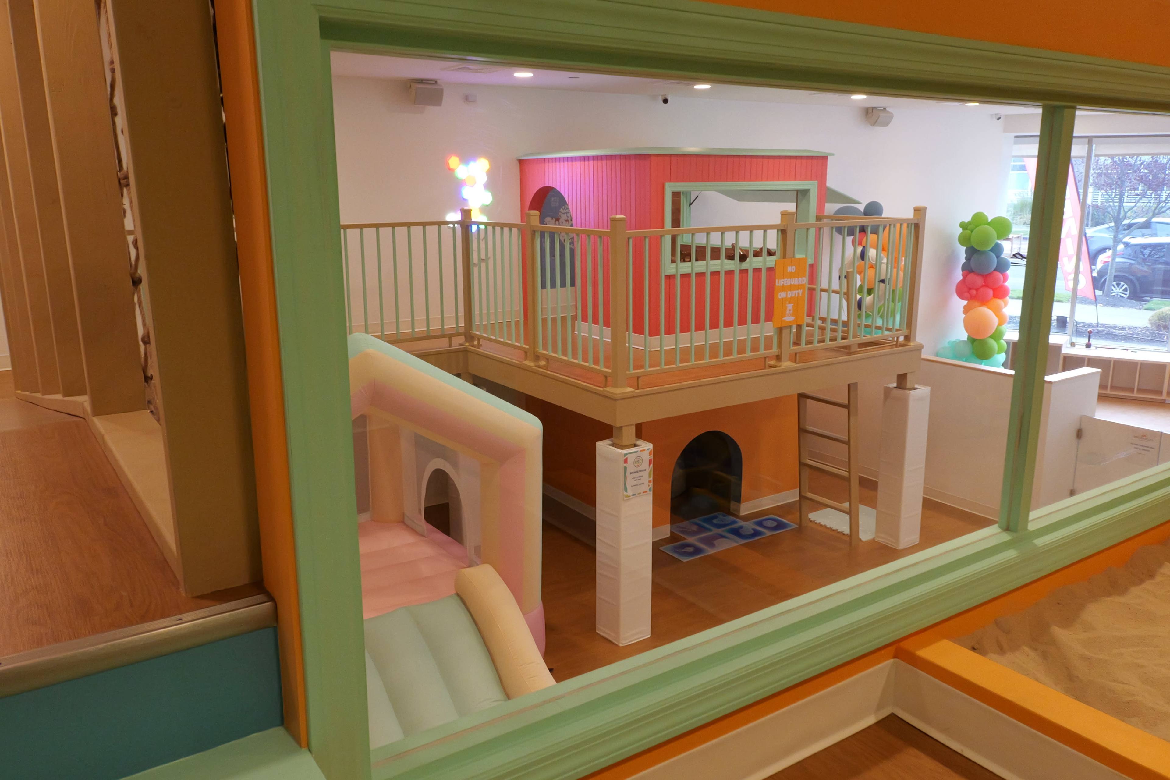 The image shows a colorful children's play area featuring a multi-level structure with slides, a staircase, and various interactive elements.